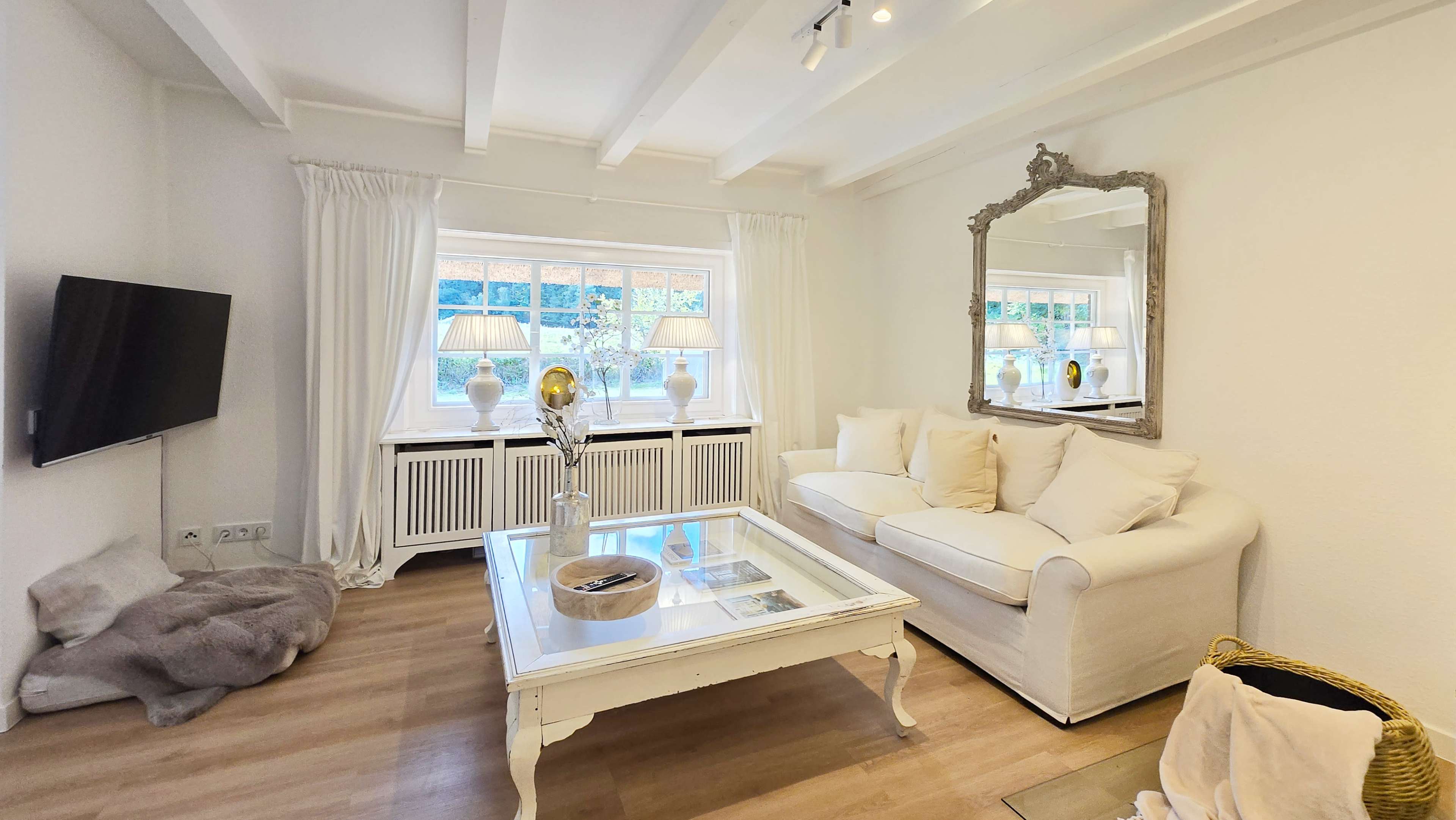 The living room features a white sofa, a glass coffee table, and large windows with white curtains, complemented by decorative lamps.