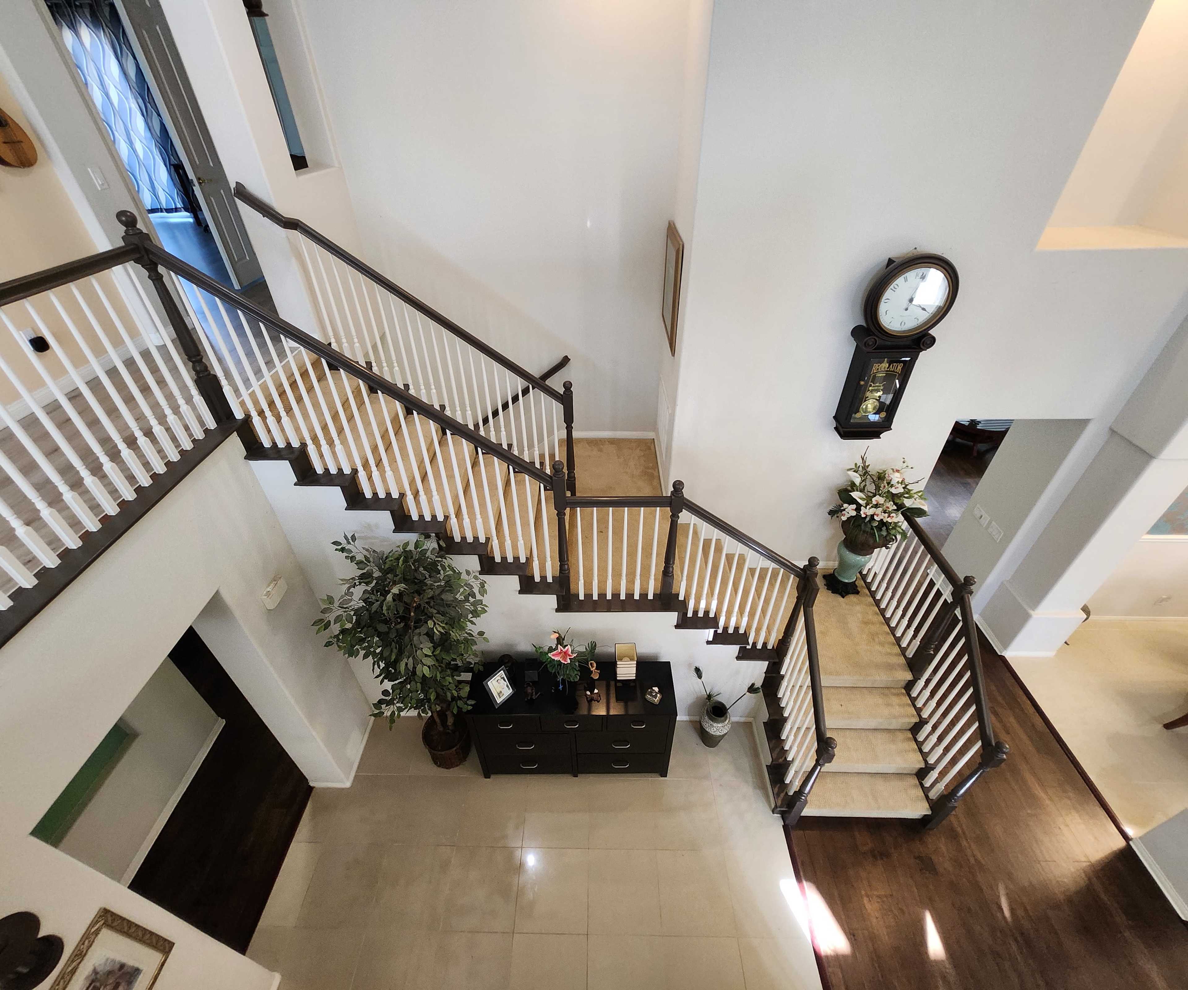 A spacious entryway with a staircase, white railings, a dark wooden floor, and decorative elements including a plant and a clock.