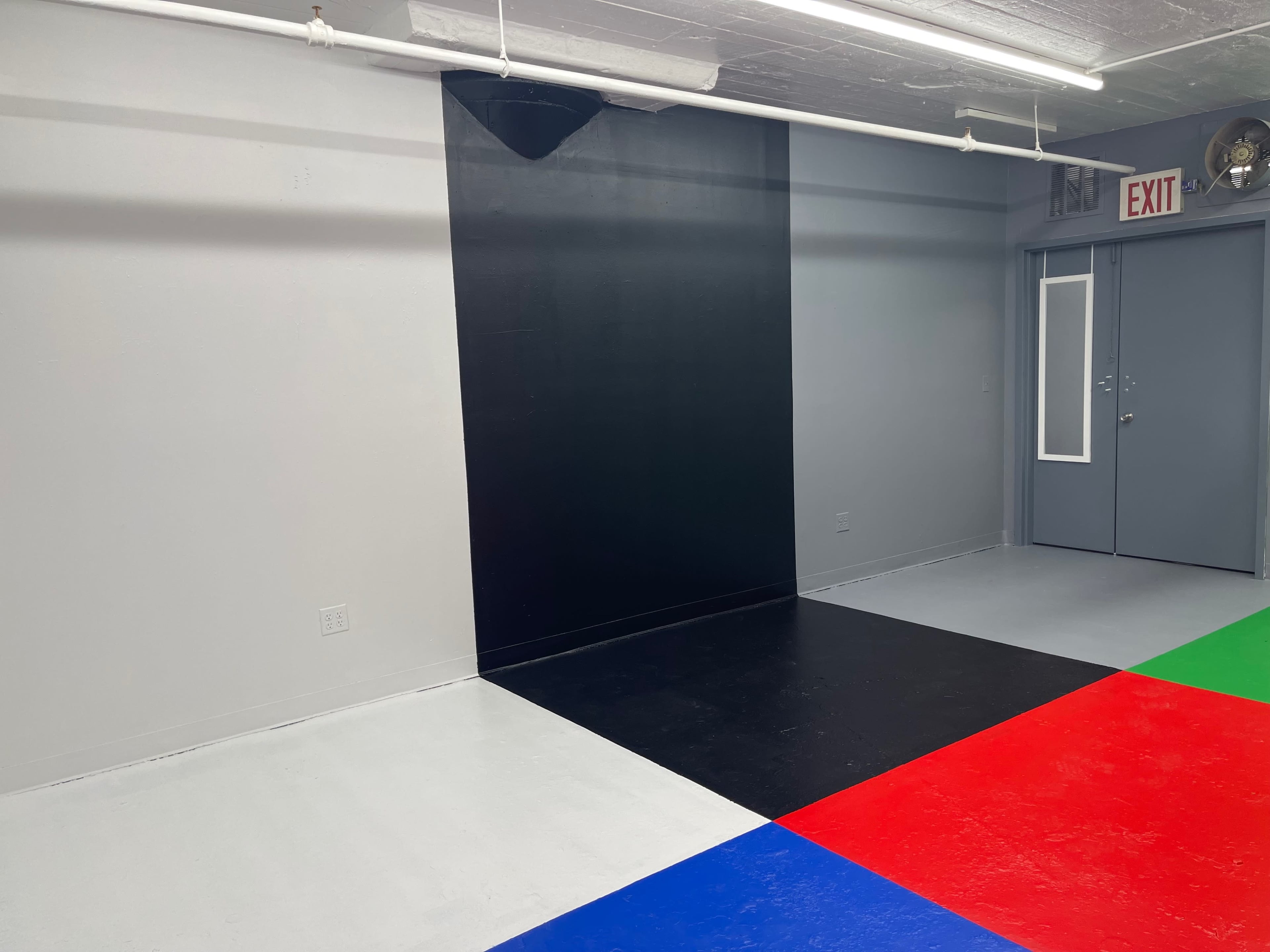 A room with a gray wall featuring a large black section and a floor divided into four colored sections: red, blue, green, and black.