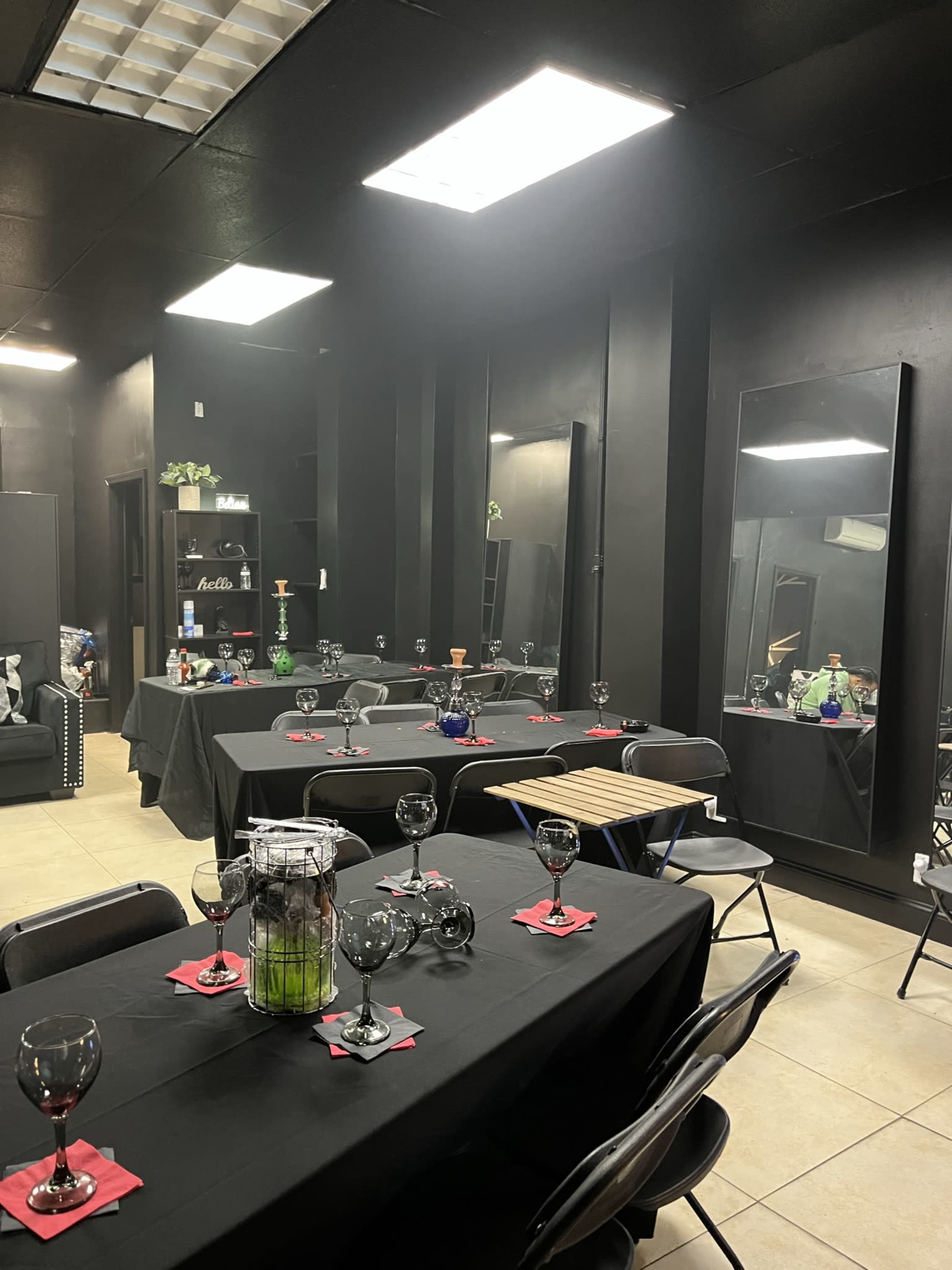 A dimly lit black room with several tables set for an event, featuring black tablecloths and glassware.