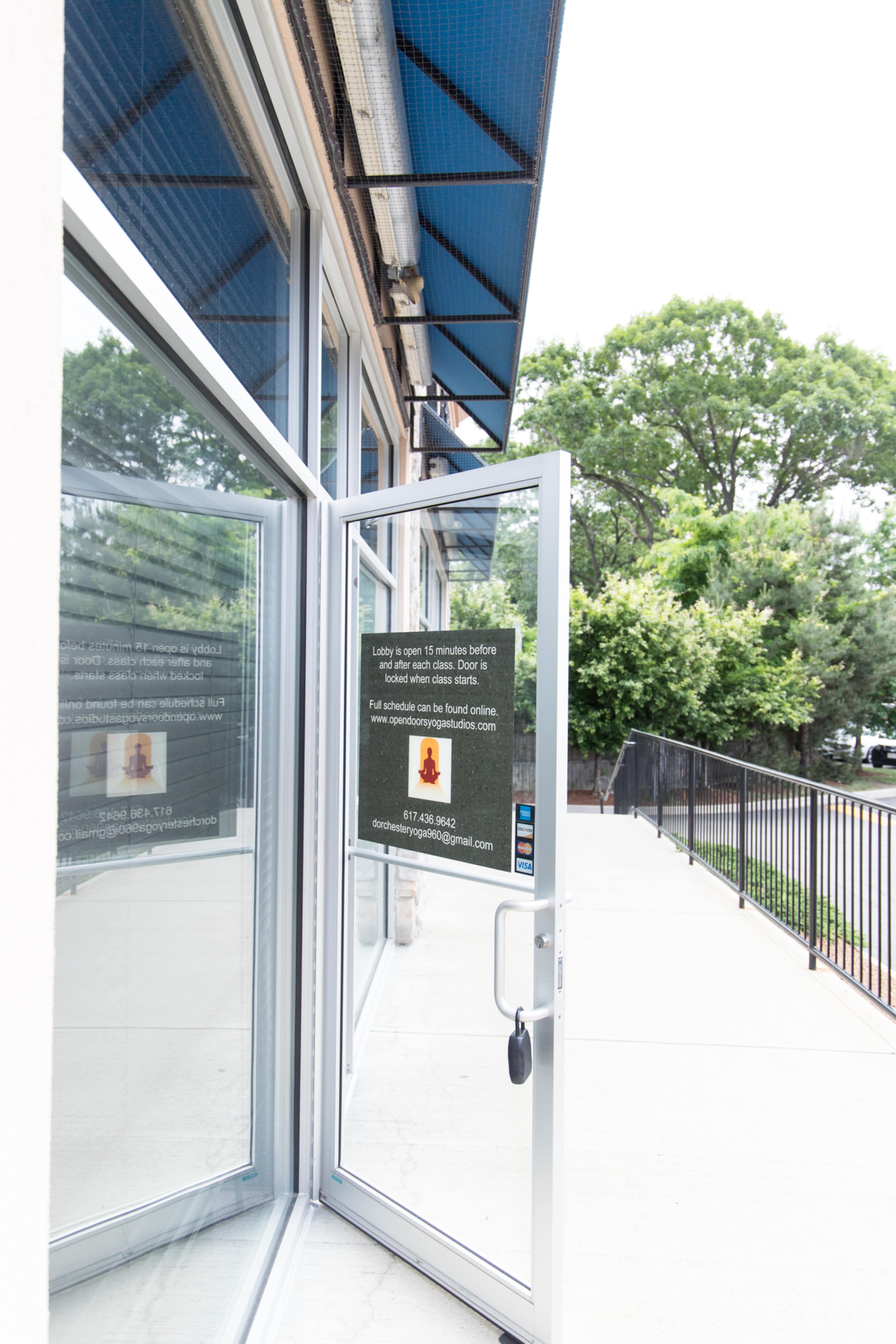 An open glass door leading to an outdoor area, with a notice poster displayed on the door.