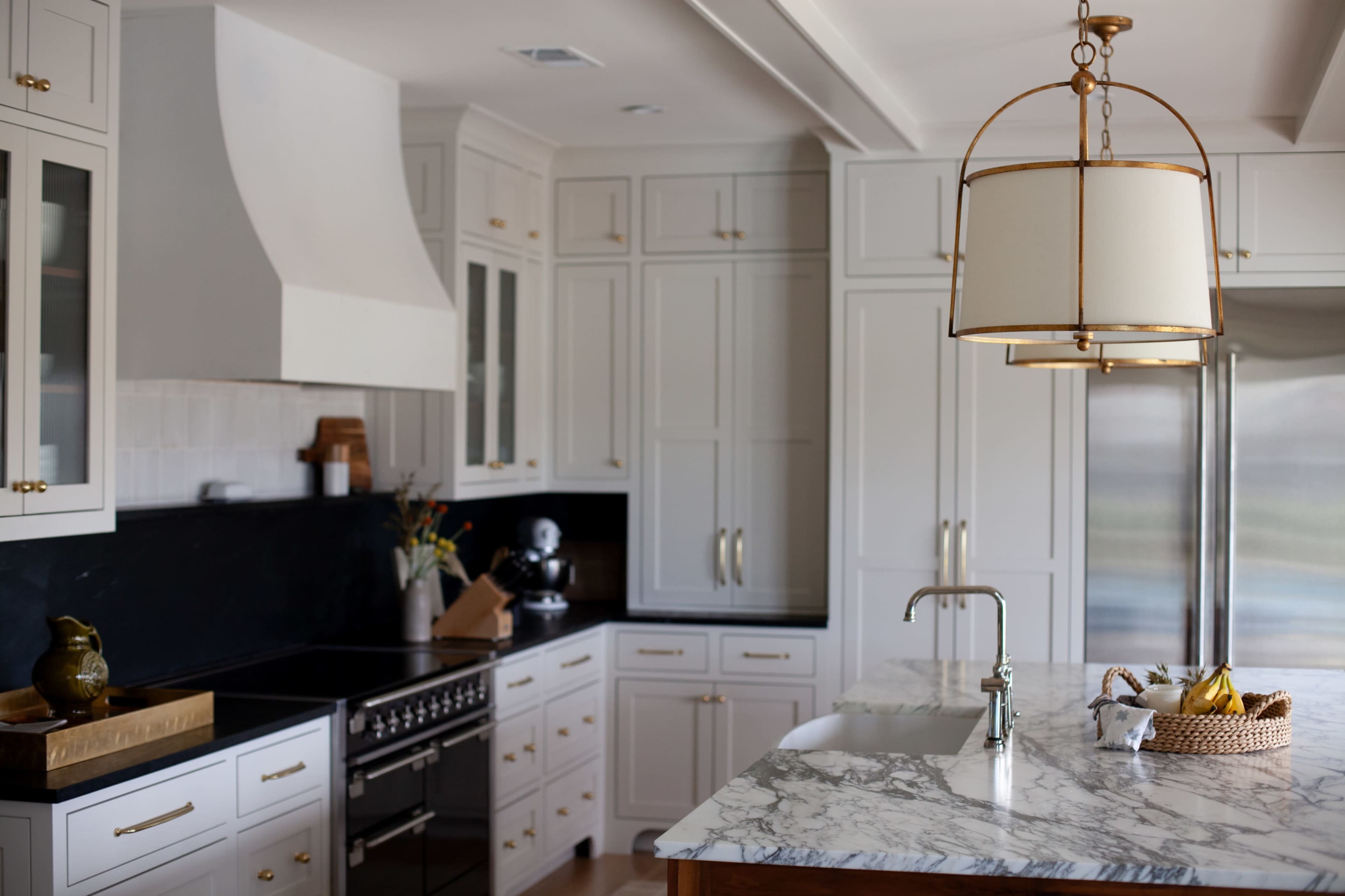 The image shows a modern kitchen featuring white cabinetry, a marble countertop, a stainless steel refrigerator, and a pendant light positioned over the island.