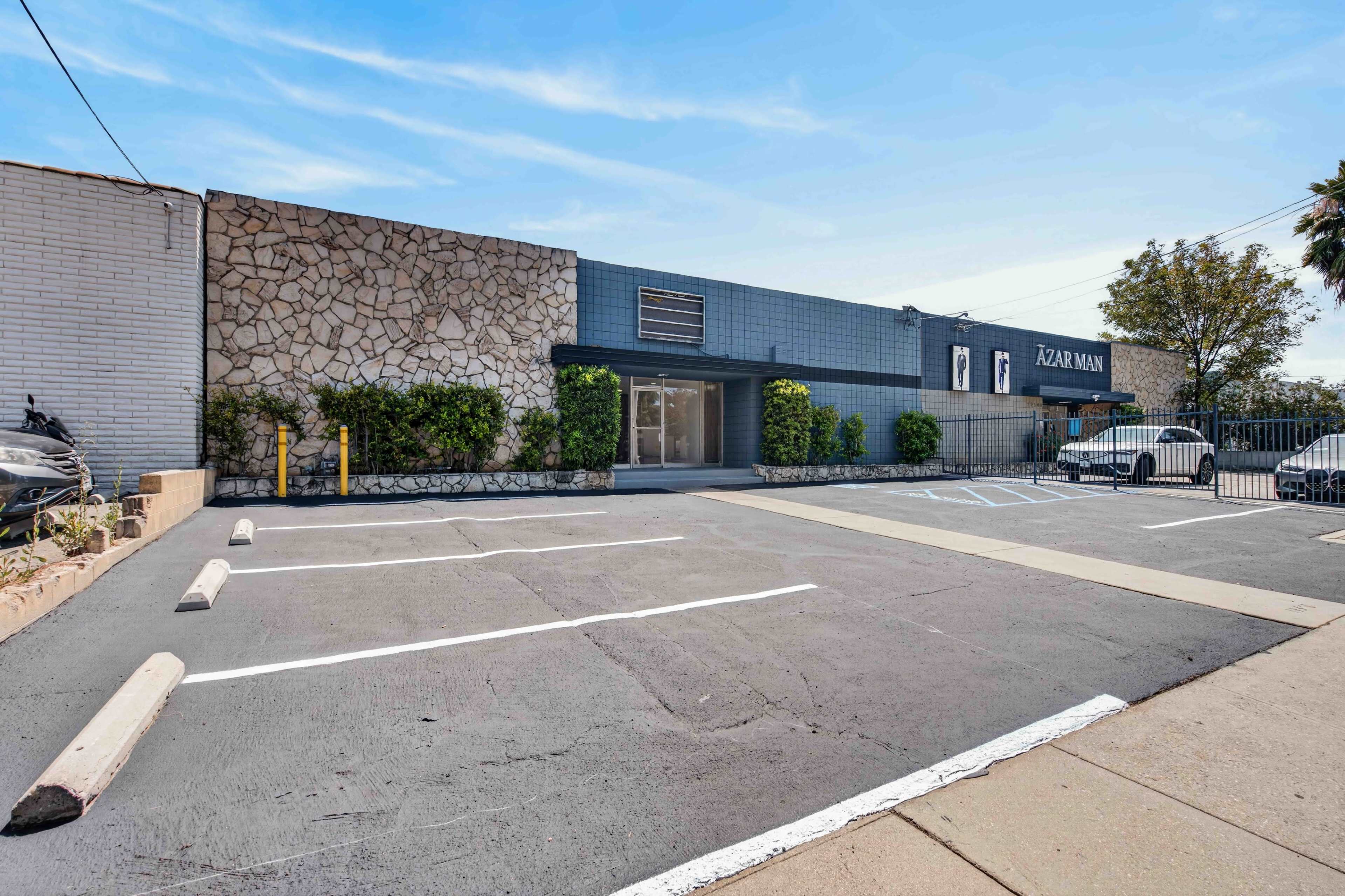 The image shows a modern commercial building with a stone accent wall, surrounded by a parking lot that has several empty spaces.
