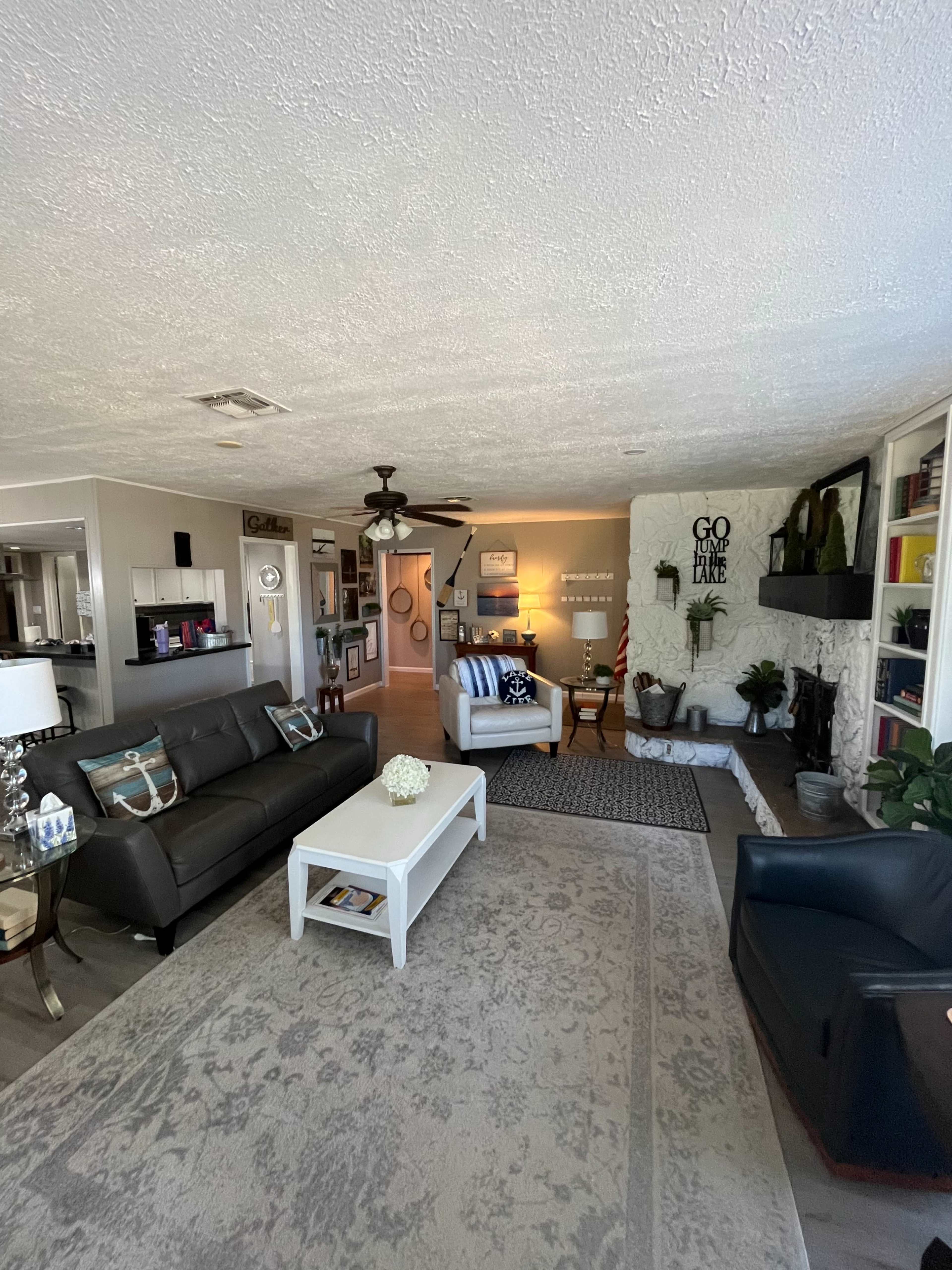 The image shows a spacious living room with a mix of modern and cozy furnishings, including a dark sofa, a white coffee table, and a decorative fireplace.