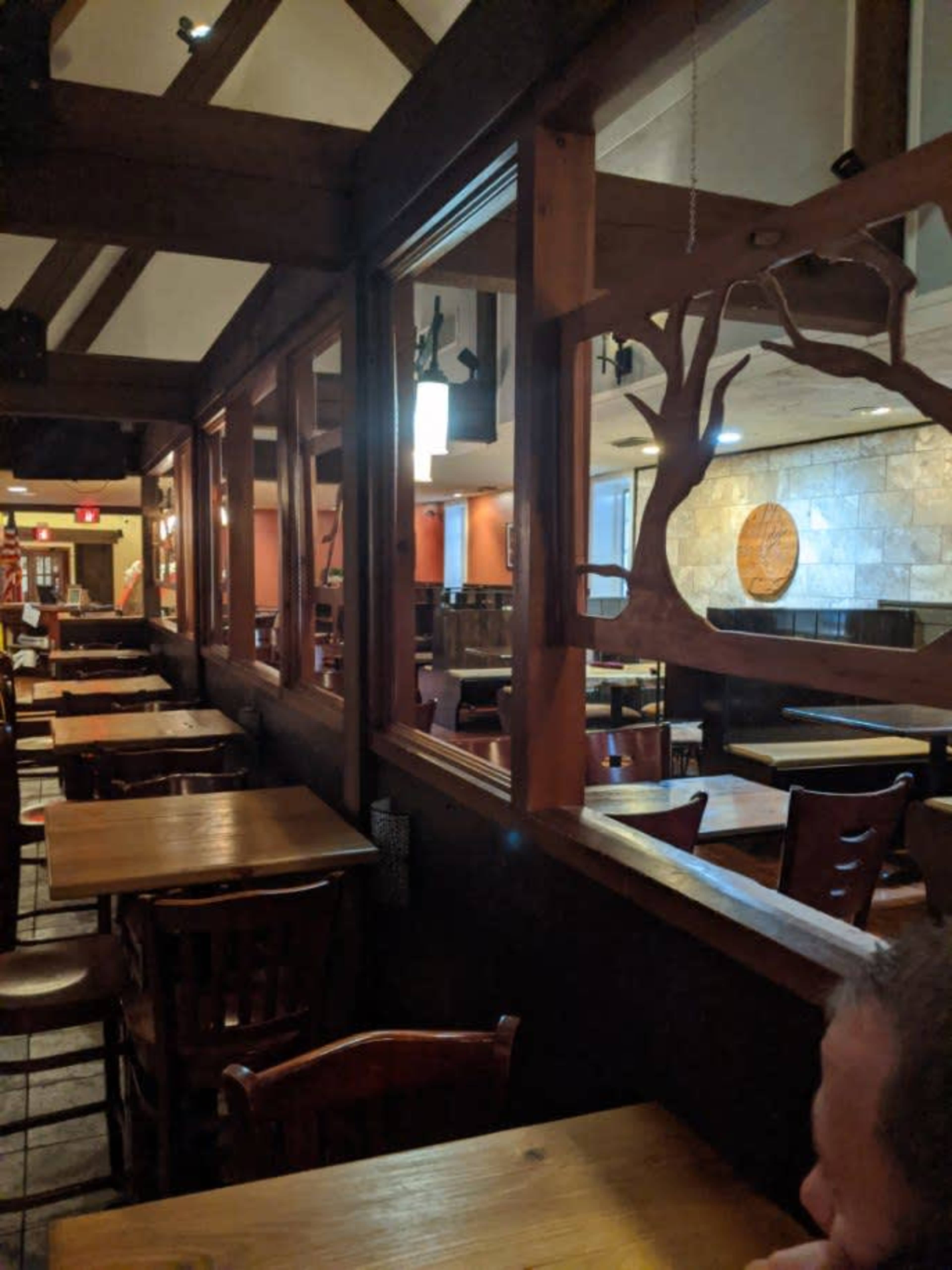 The interior of a restaurant with wooden tables and chairs, separated by wooden partitions featuring a tree design, and lit by hanging lights.