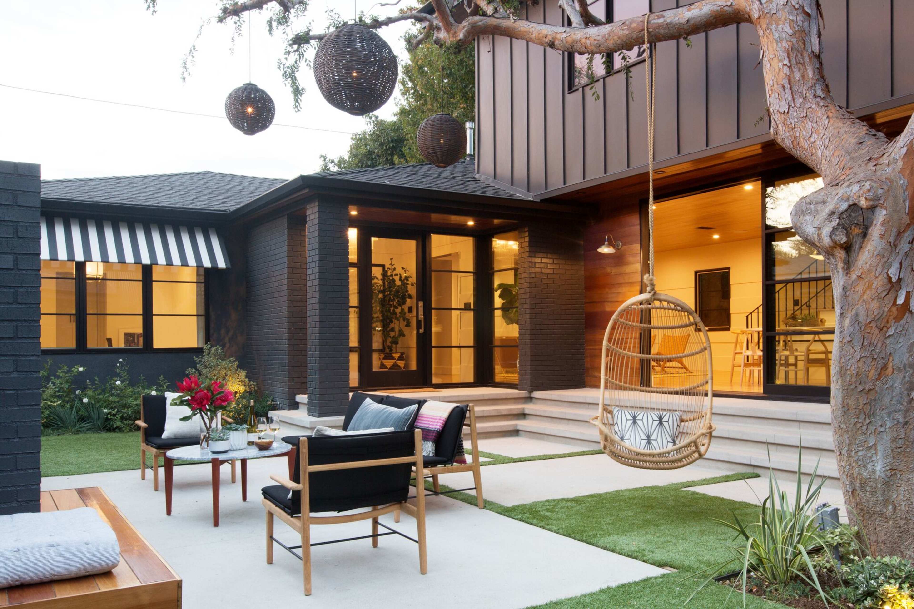 A modern outdoor patio area featuring a hanging chair, seating arrangement, and decorative plants around a contemporary home.