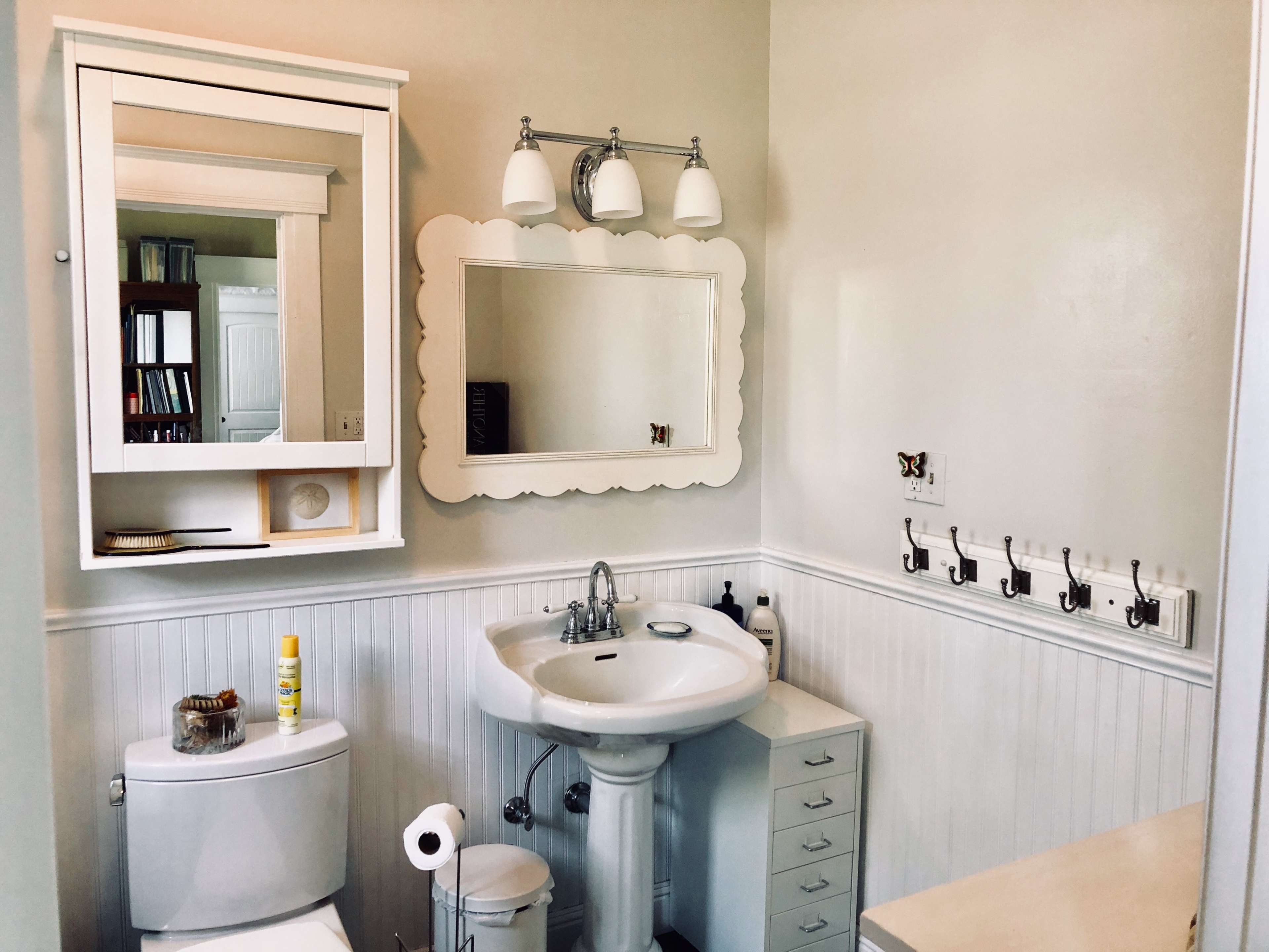 A small, well-organized bathroom featuring a sink with a mirror above it, a toilet, and a set of hooks on the wall.