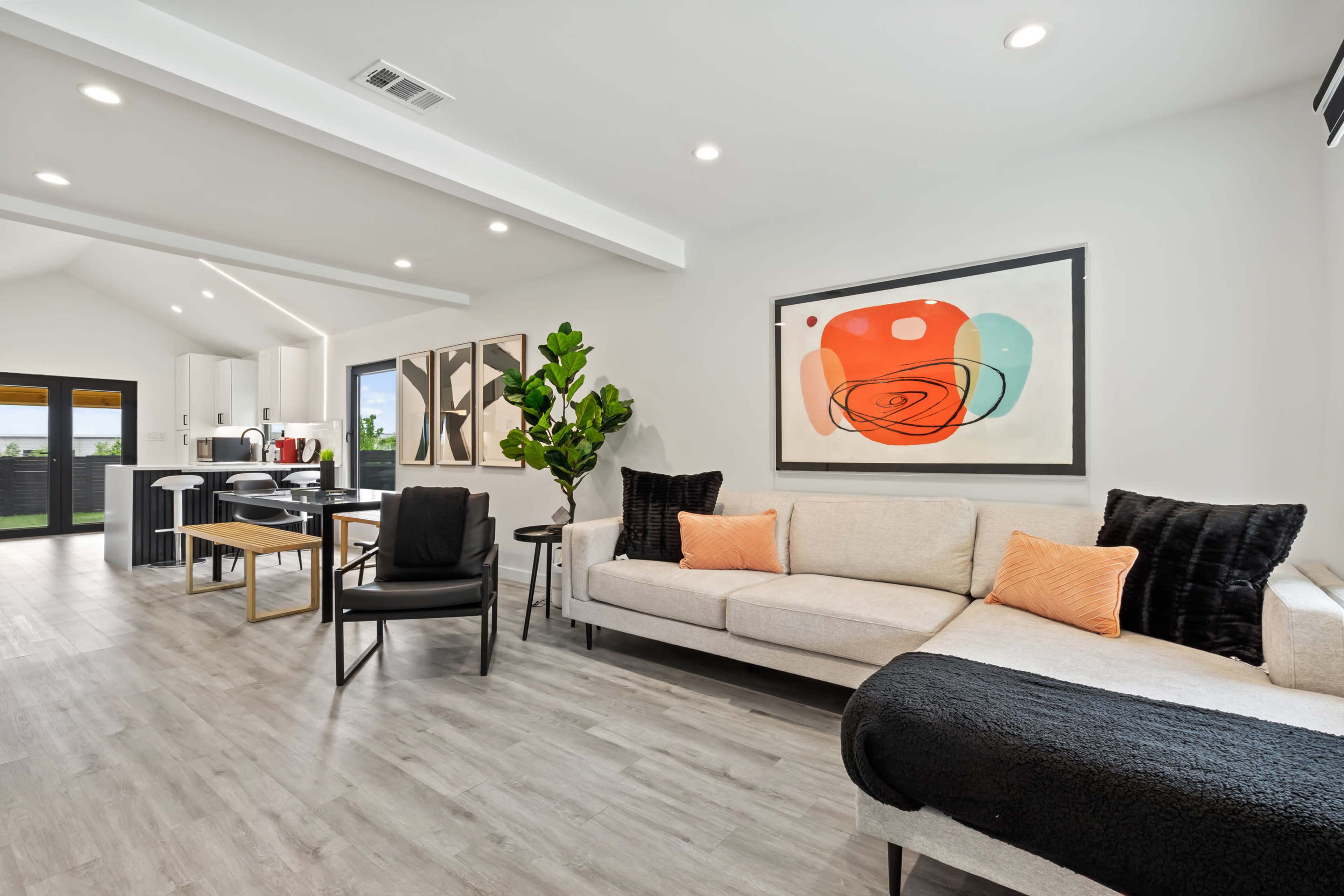 A modern living room with a sectional sofa, decorative pillows, a dining area, and an abstract artwork on the wall.