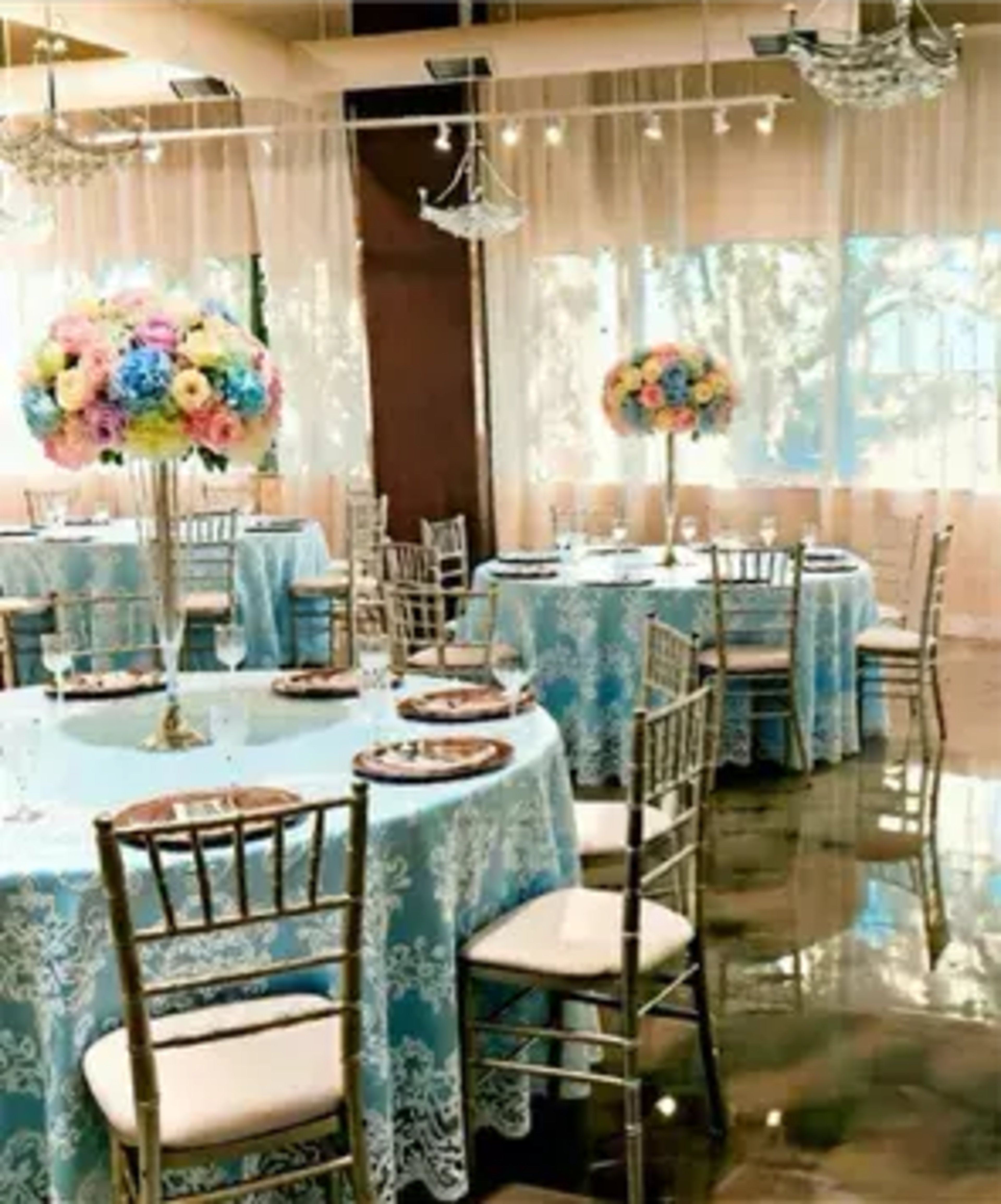A dining area features elegantly set tables with blue lace tablecloths and floral centerpieces.