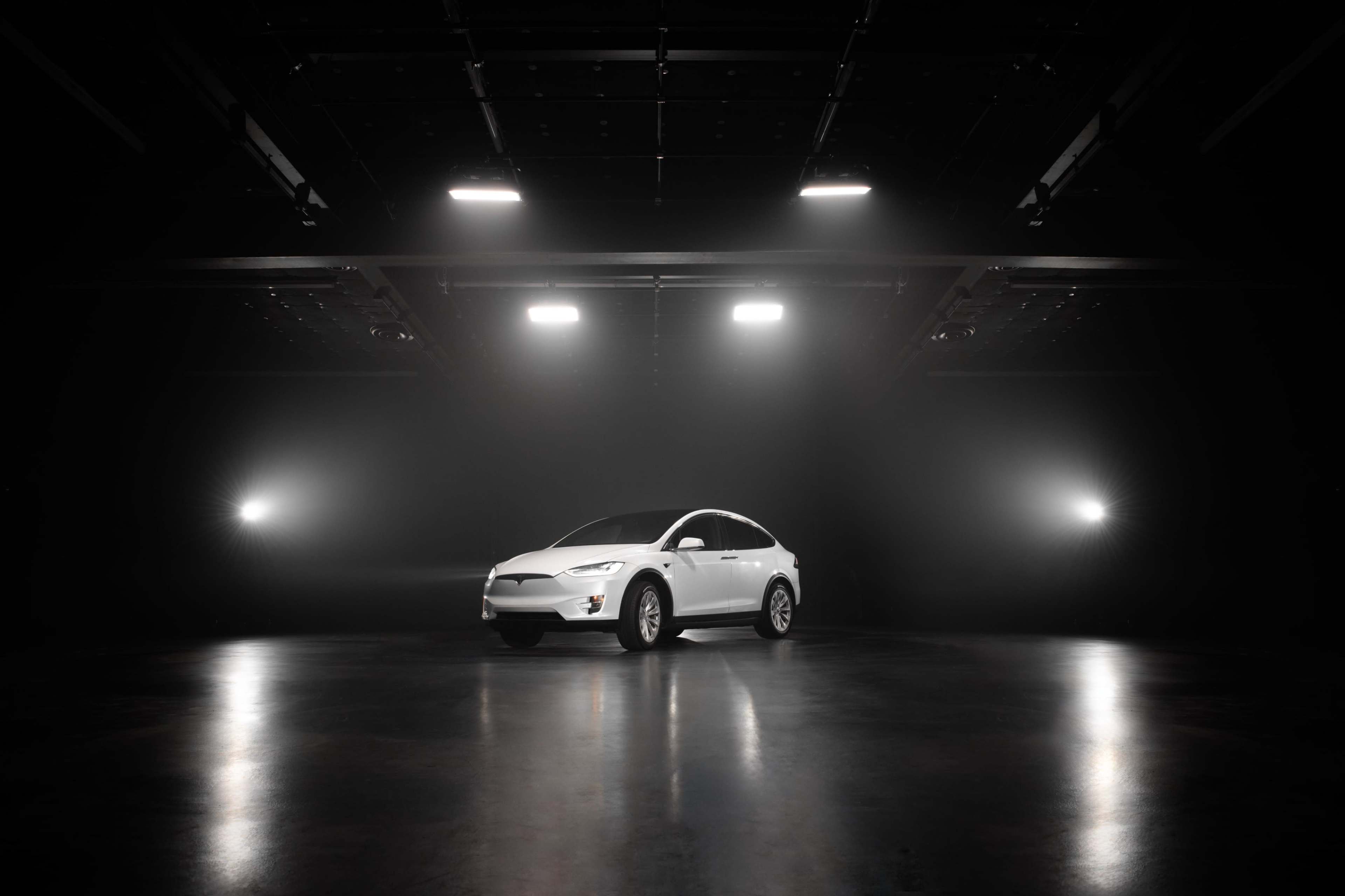 A white car is positioned in a dimly lit studio with bright lights shining from above.