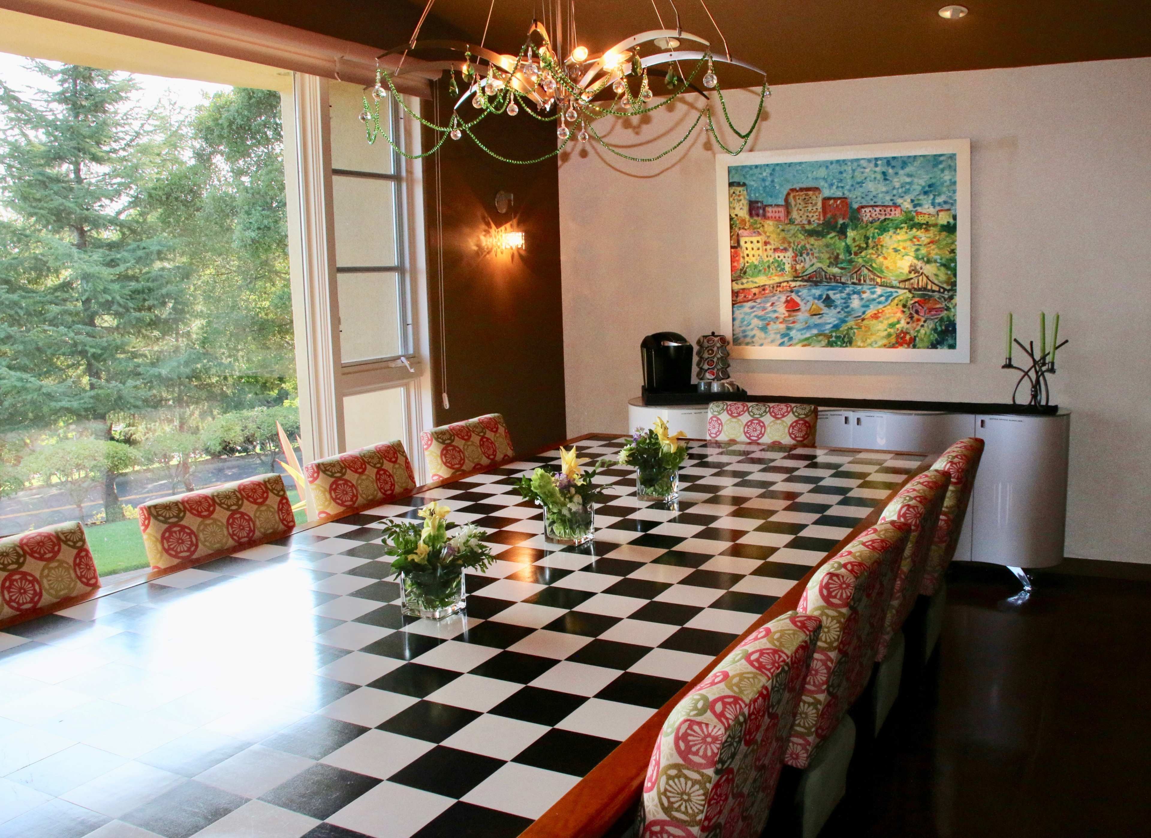The image shows a spacious dining room with a large checkered table adorned with floral centerpieces and surrounded by patterned chairs.
