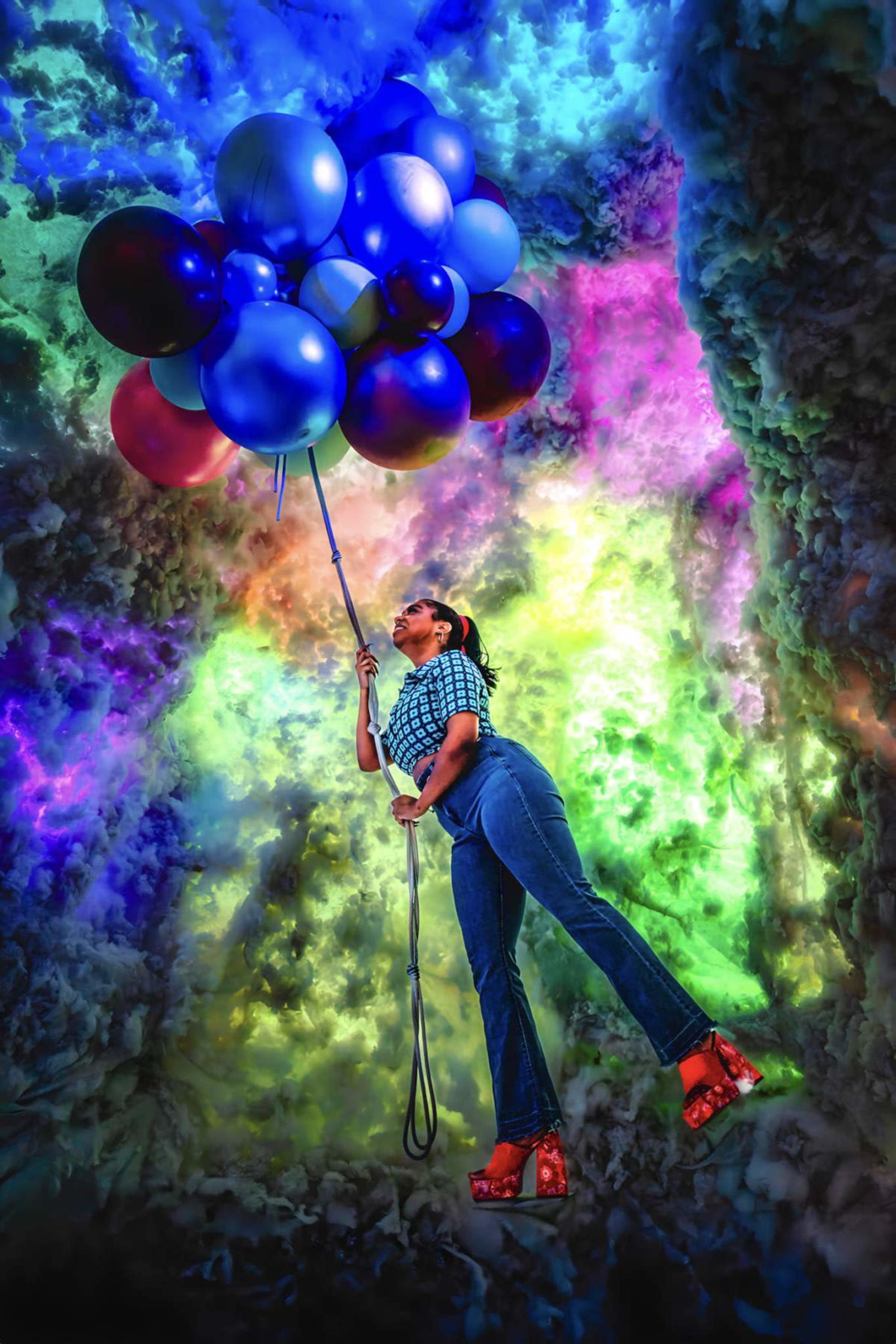A woman holds a cluster of colorful balloons while standing against a vibrant, abstract background.