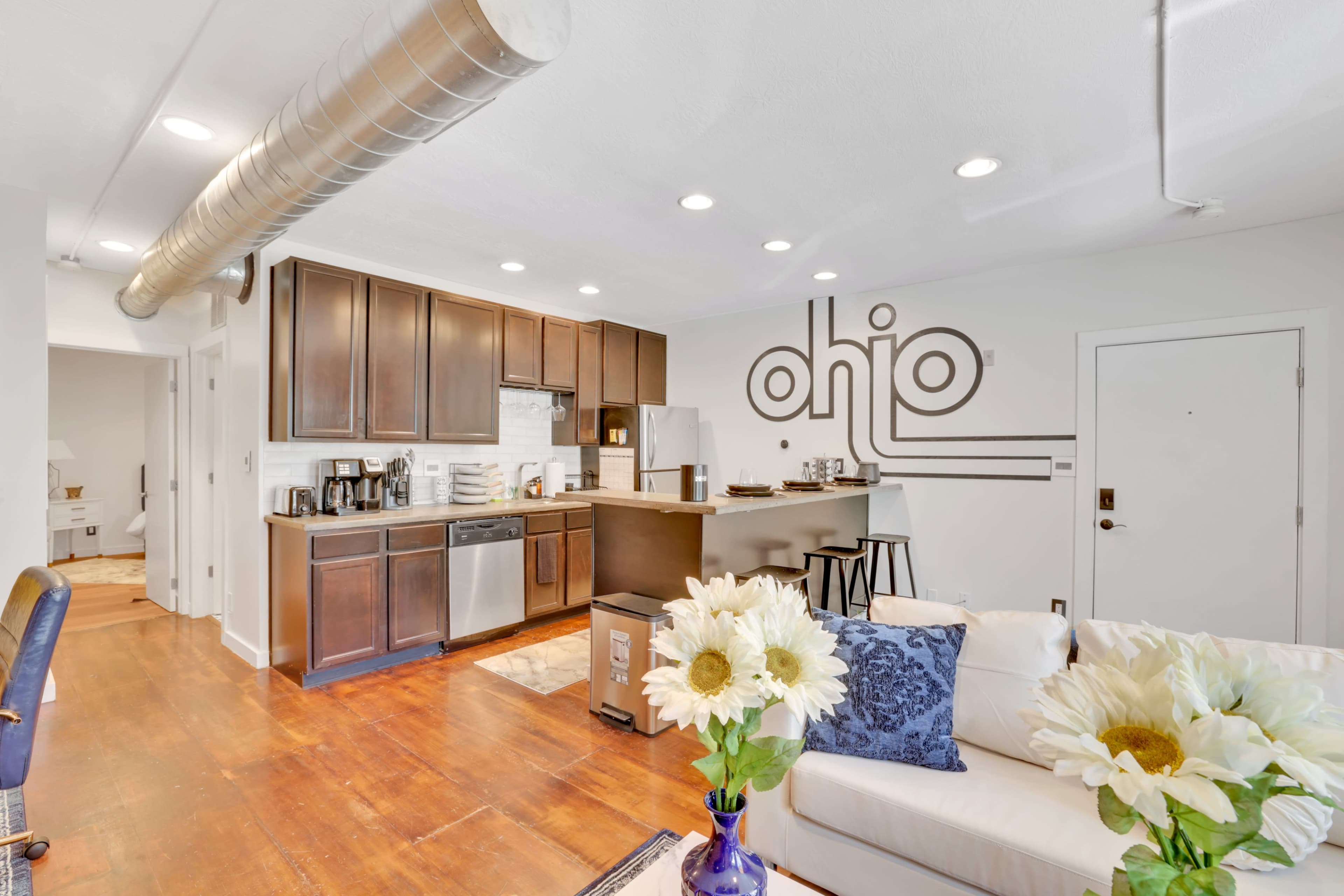 A modern kitchen and living area with wooden floors, dark cabinetry, and a wall featuring the word "Ohio."