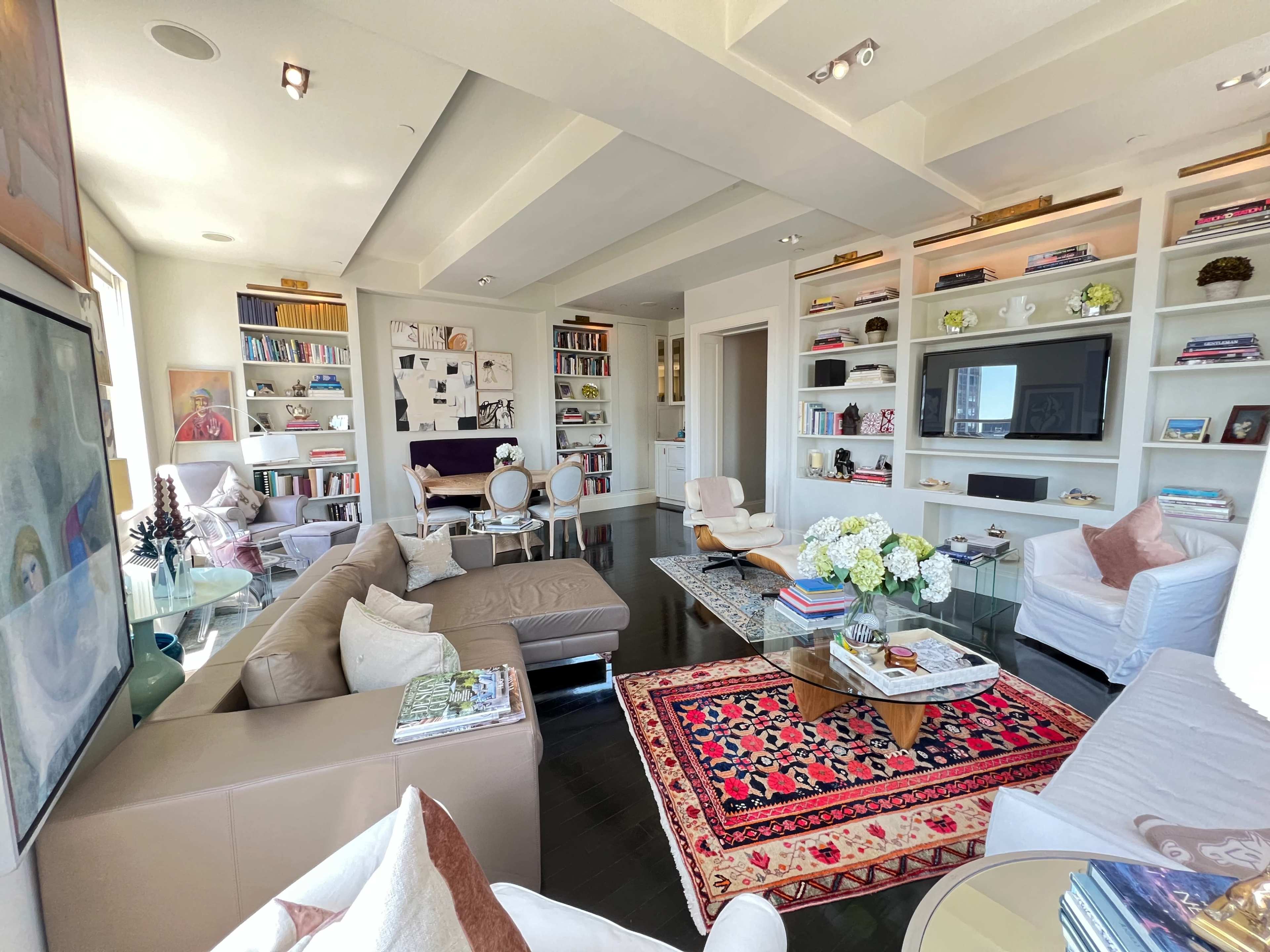 A modern living room features a spacious seating area with a large sectional sofa, an ornate rug, and built-in shelves filled with books and decorative items.
