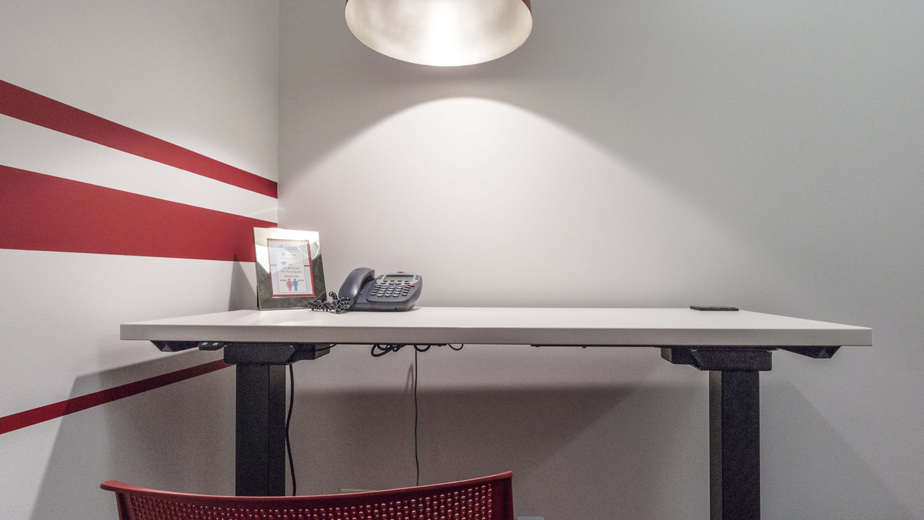 A modern desk with a phone and a framed item is positioned against a wall featuring red stripes.