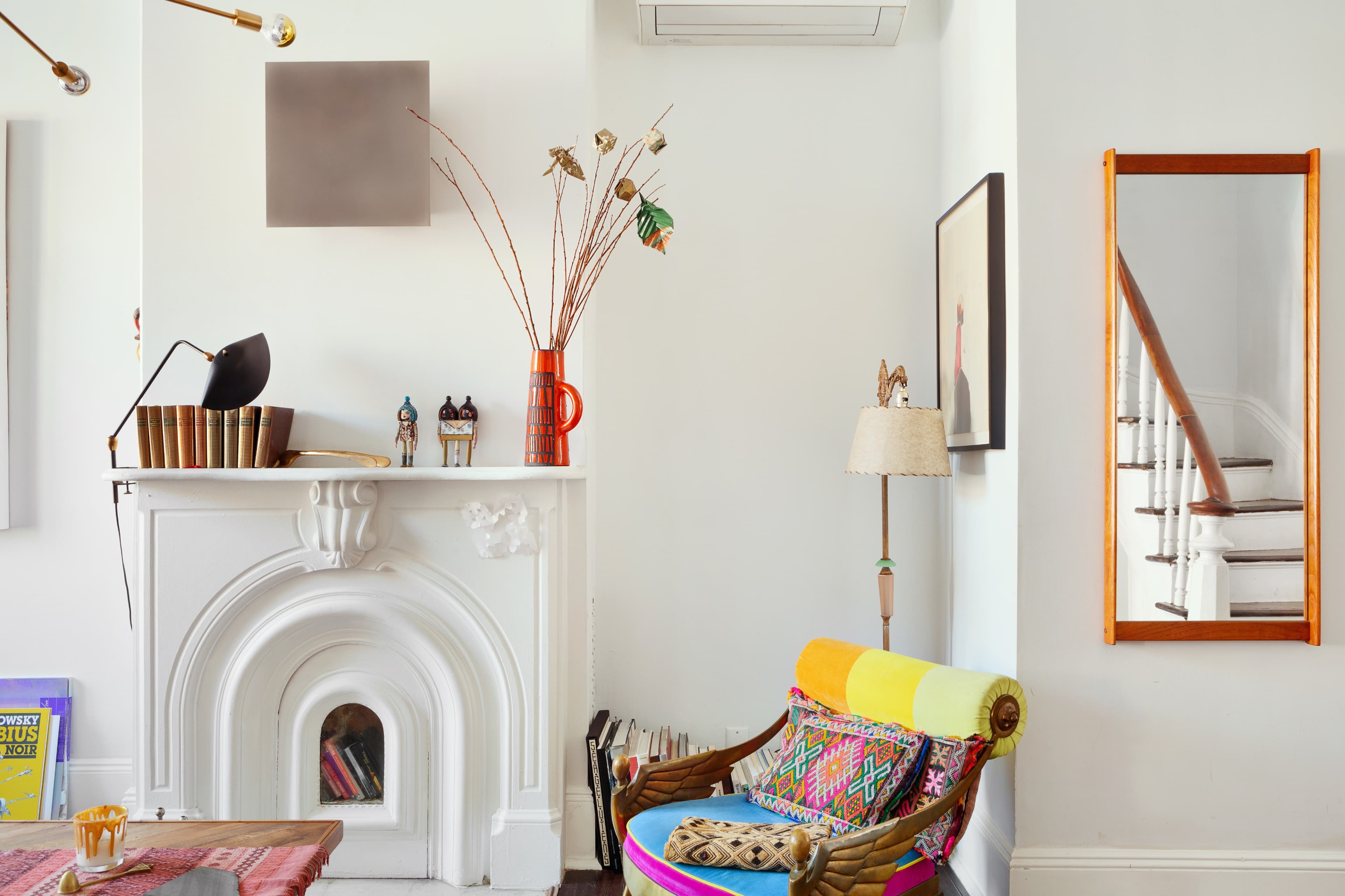 The image features a living room with a colorful armchair, a decorative fireplace, and a staircase visible in the background.