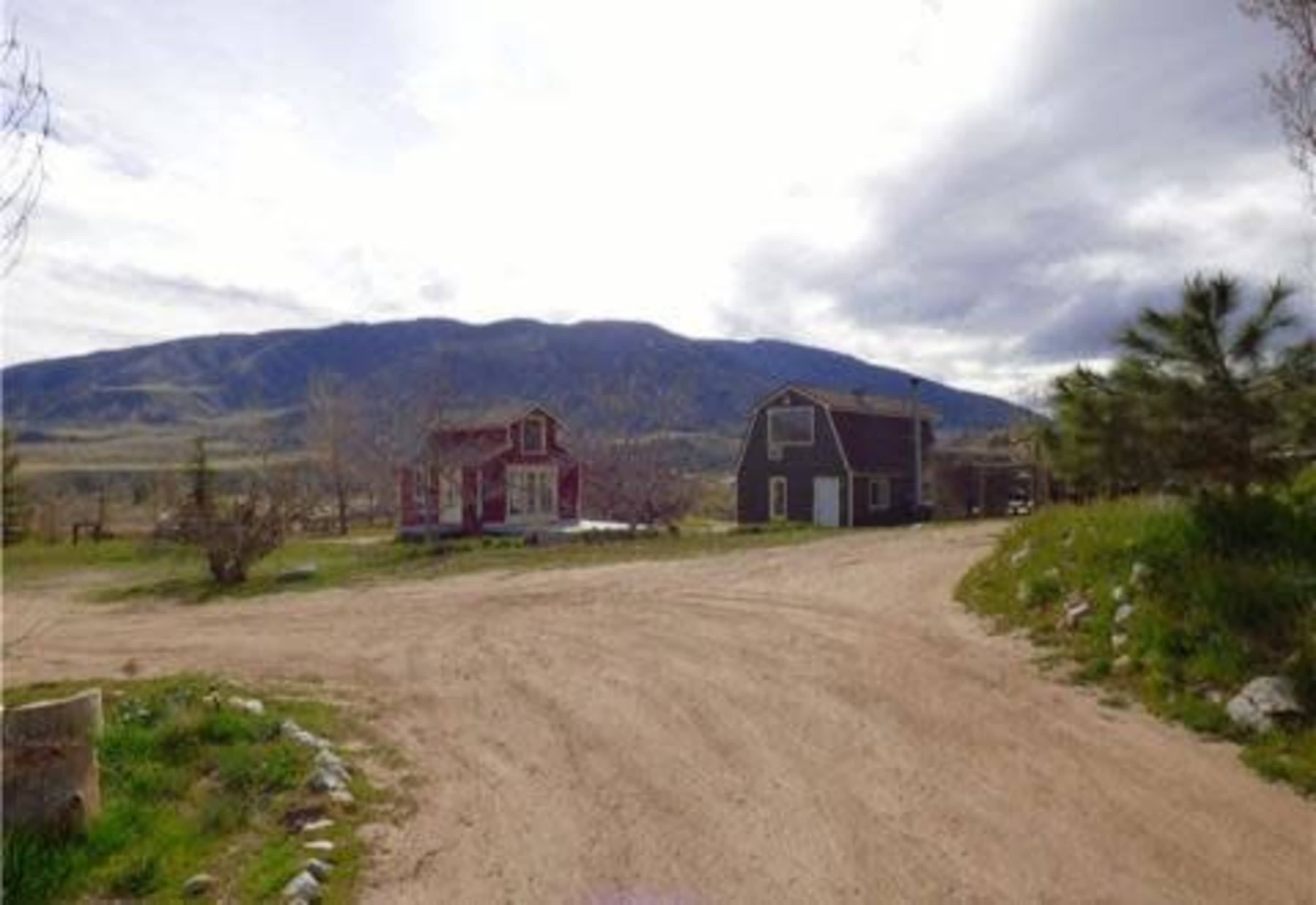 A dirt road diverges between two houses, with a mountainous landscape in the background.