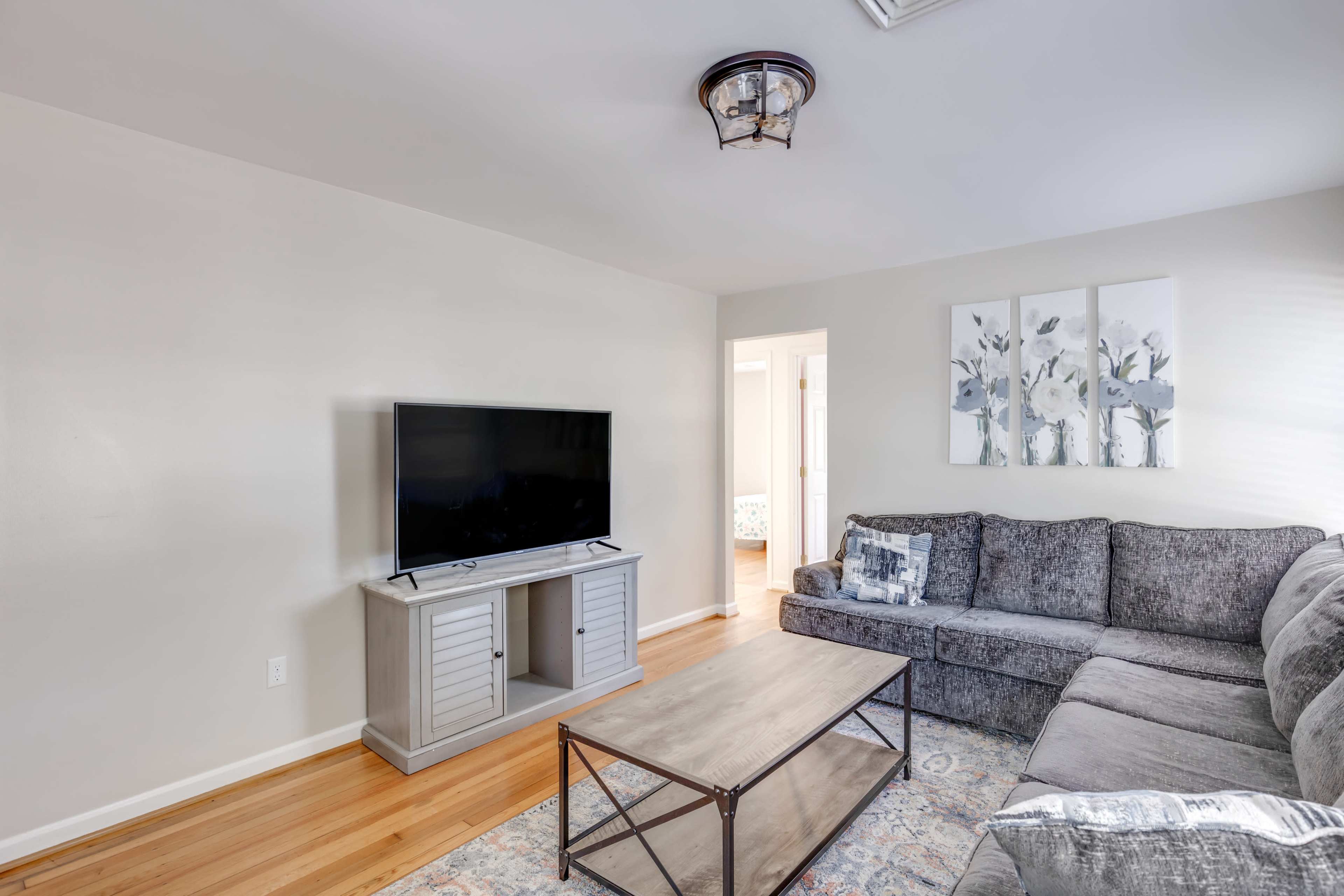 A living room with a large television mounted on a wall unit, a gray sectional sofa, and a coffee table on a patterned rug.