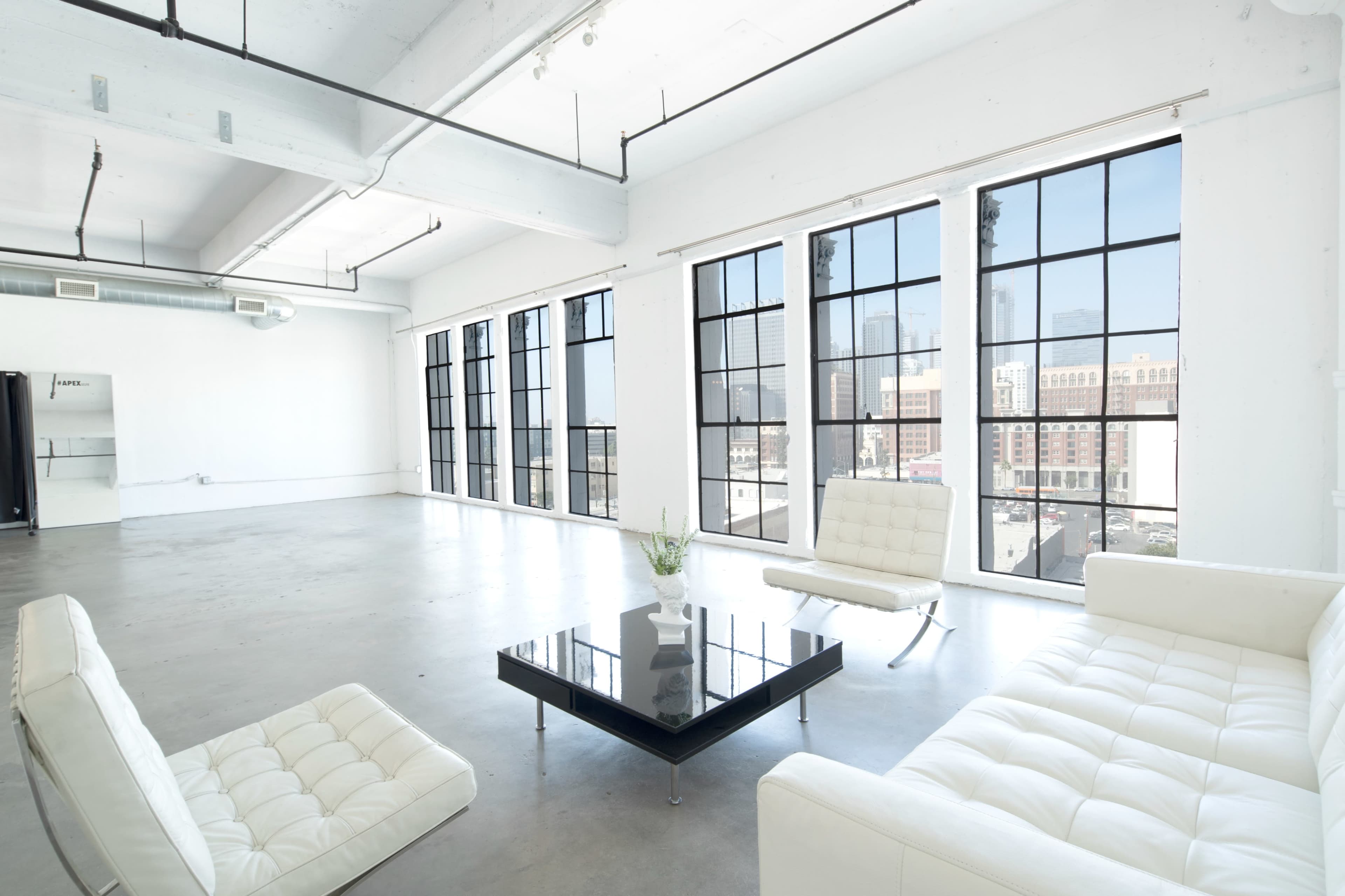 A spacious, minimalist room with large windows, concrete floors, and modern furniture including a white sofa and a black coffee table.