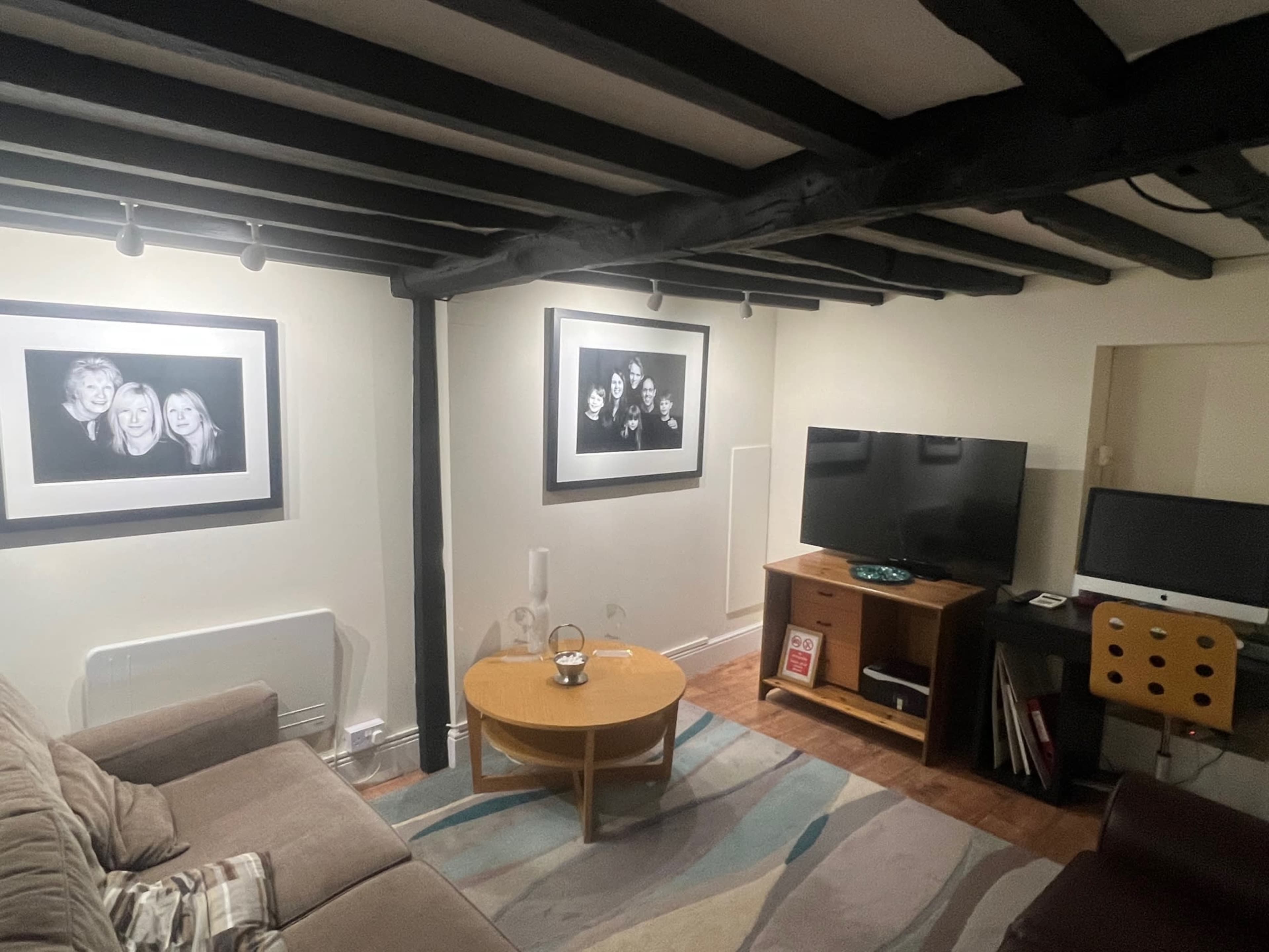 A cozy living room with a sofa, a round coffee table, two black-and-white framed photos on the walls, and a television mounted on a wooden cabinet.