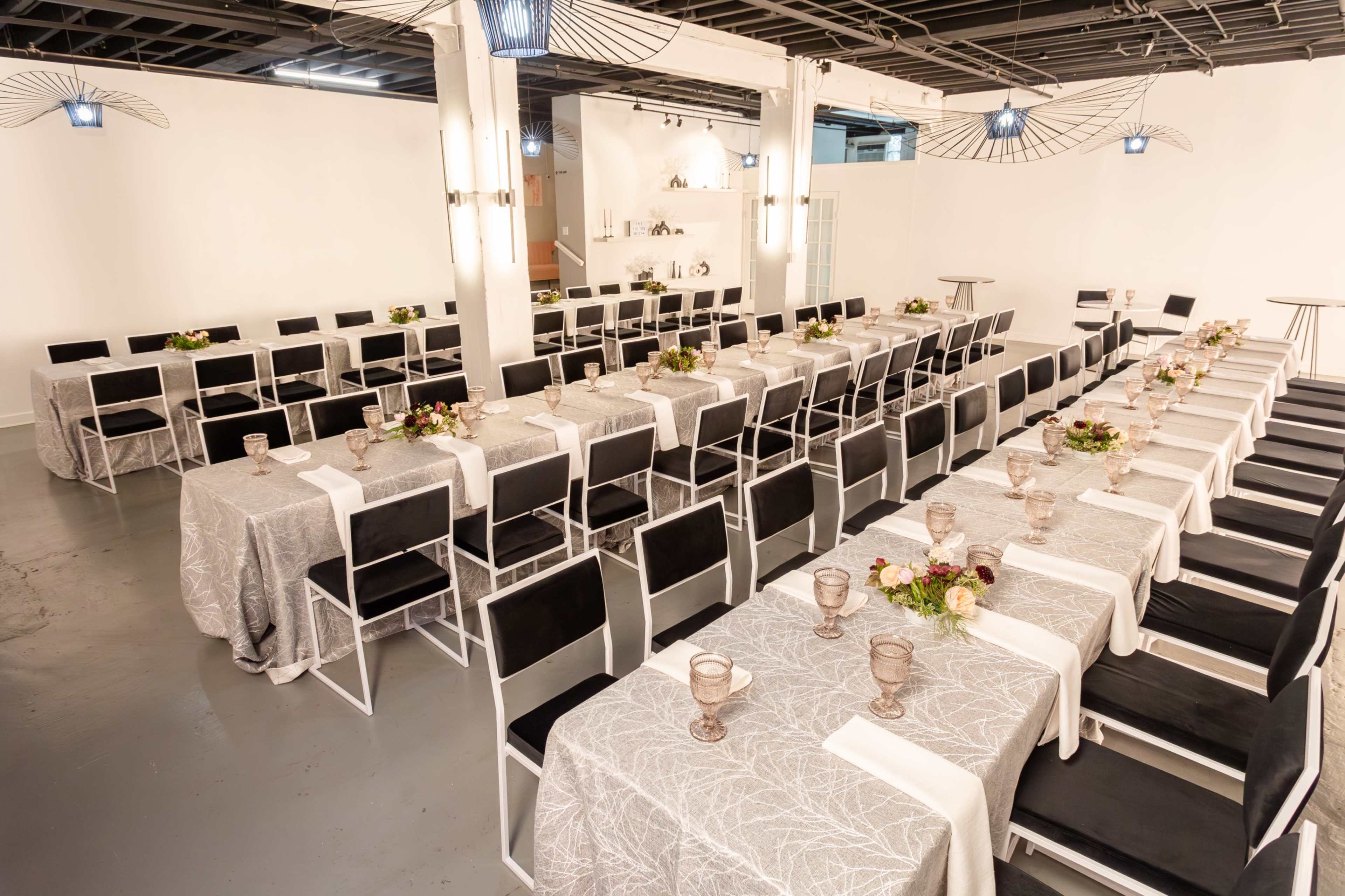 A large event space is set up with several rows of tables covered in patterned tablecloths and decorated with floral arrangements.