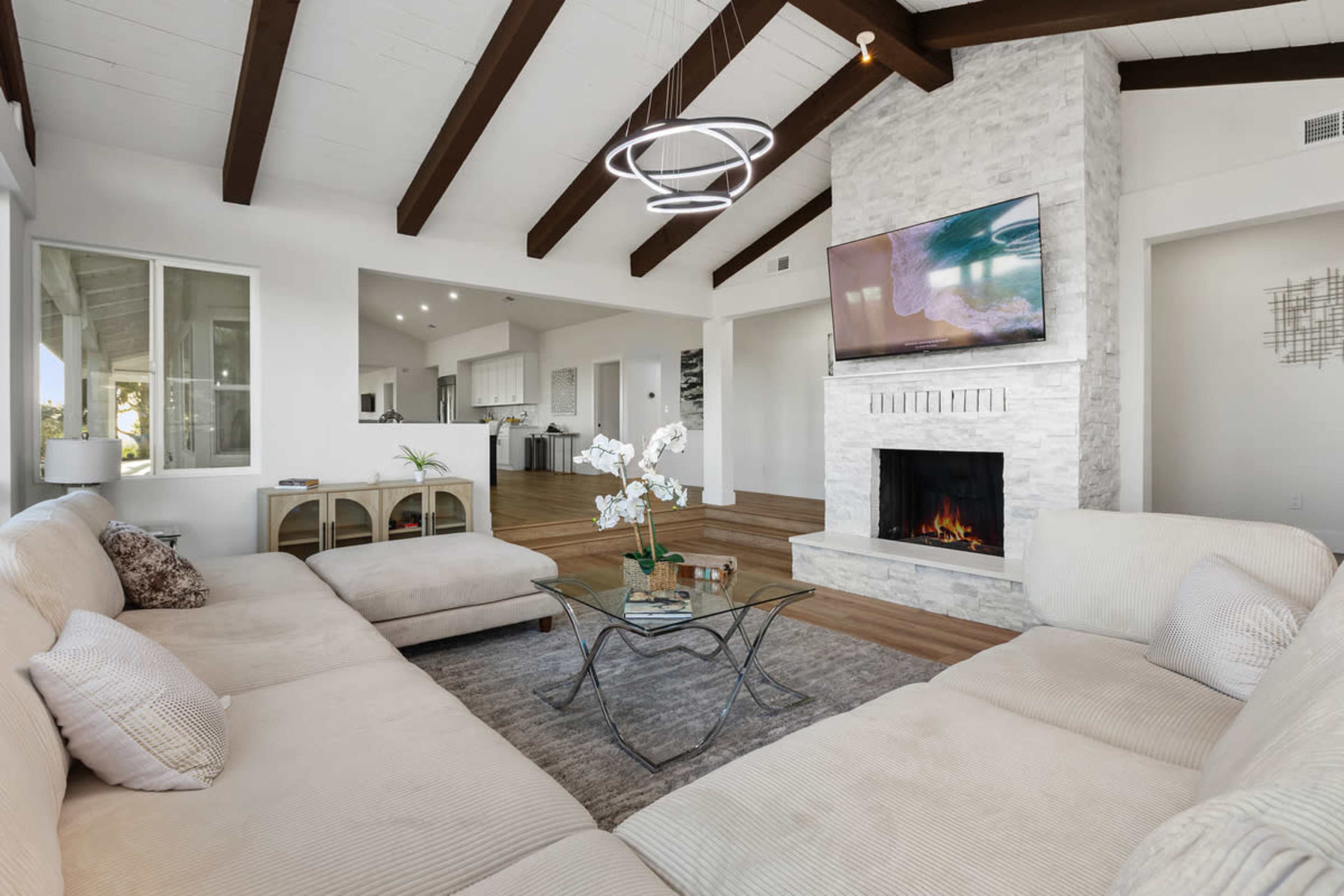 The image shows a modern living room with a sectional sofa, a coffee table, a stone fireplace, and a mounted television.