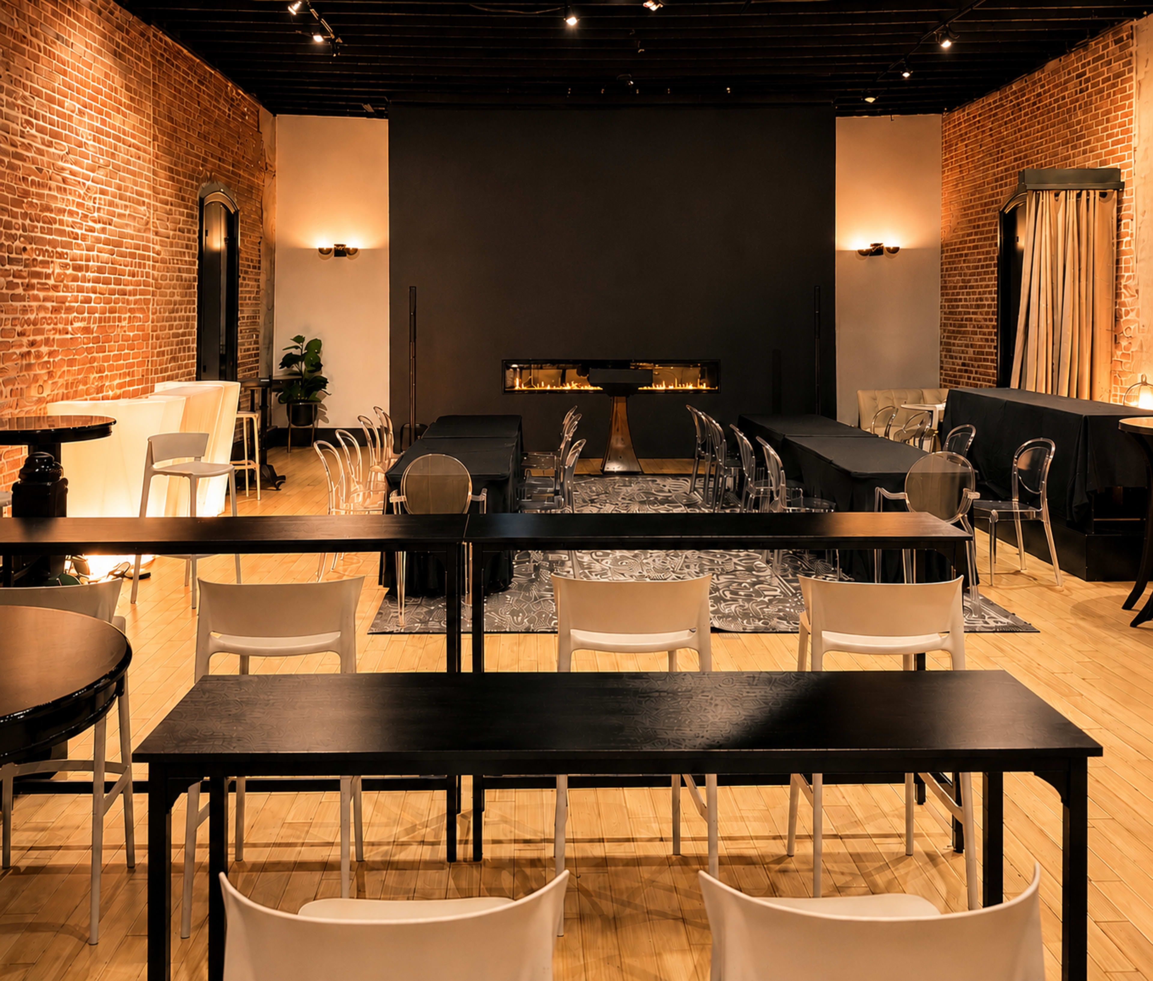 A spacious event room features rows of tables and chairs, with exposed brick walls, a dark accent wall, and a decorative fireplace.