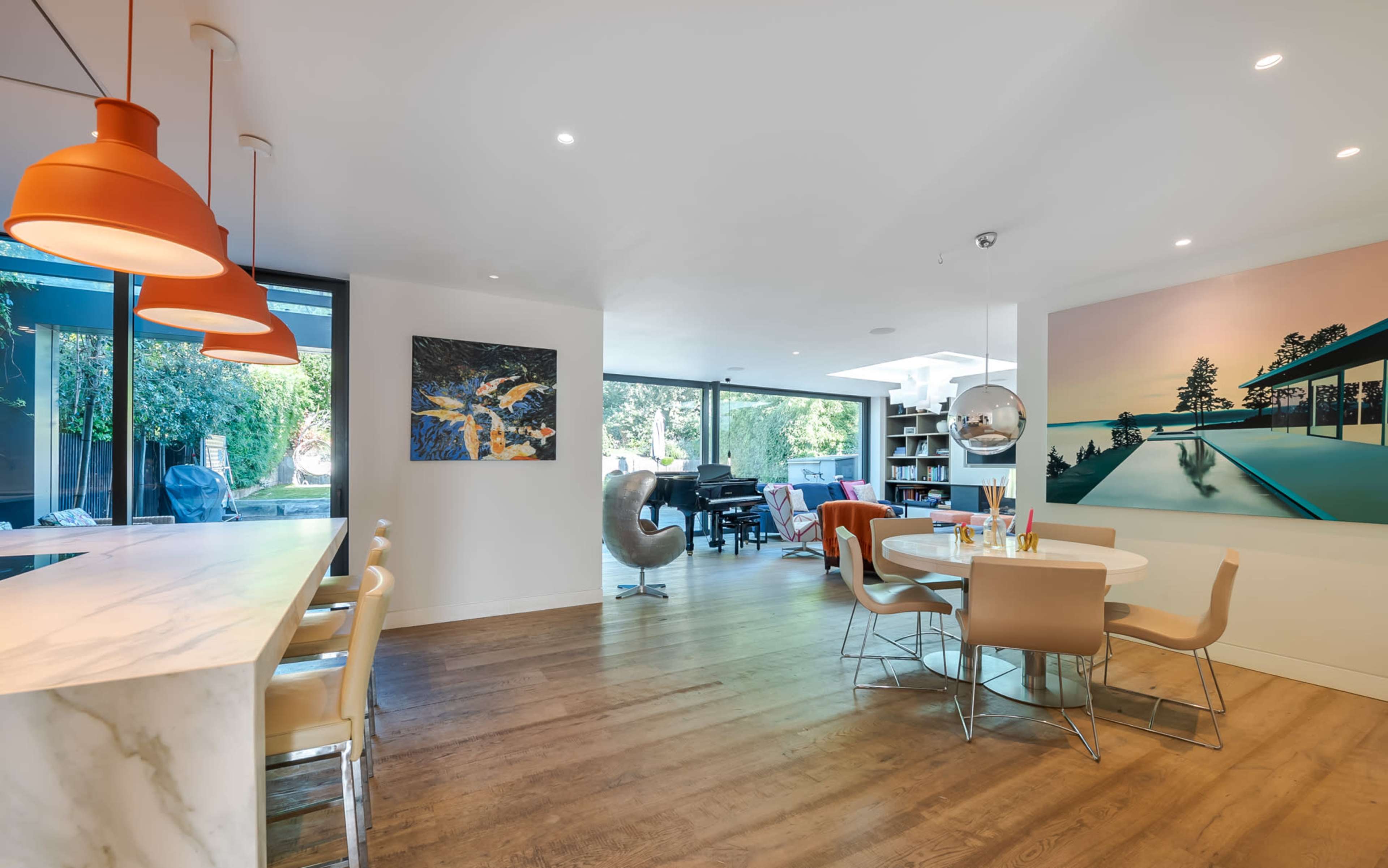 The image shows a modern living space featuring a kitchen island, a dining area with a round table, and large windows that provide natural light.