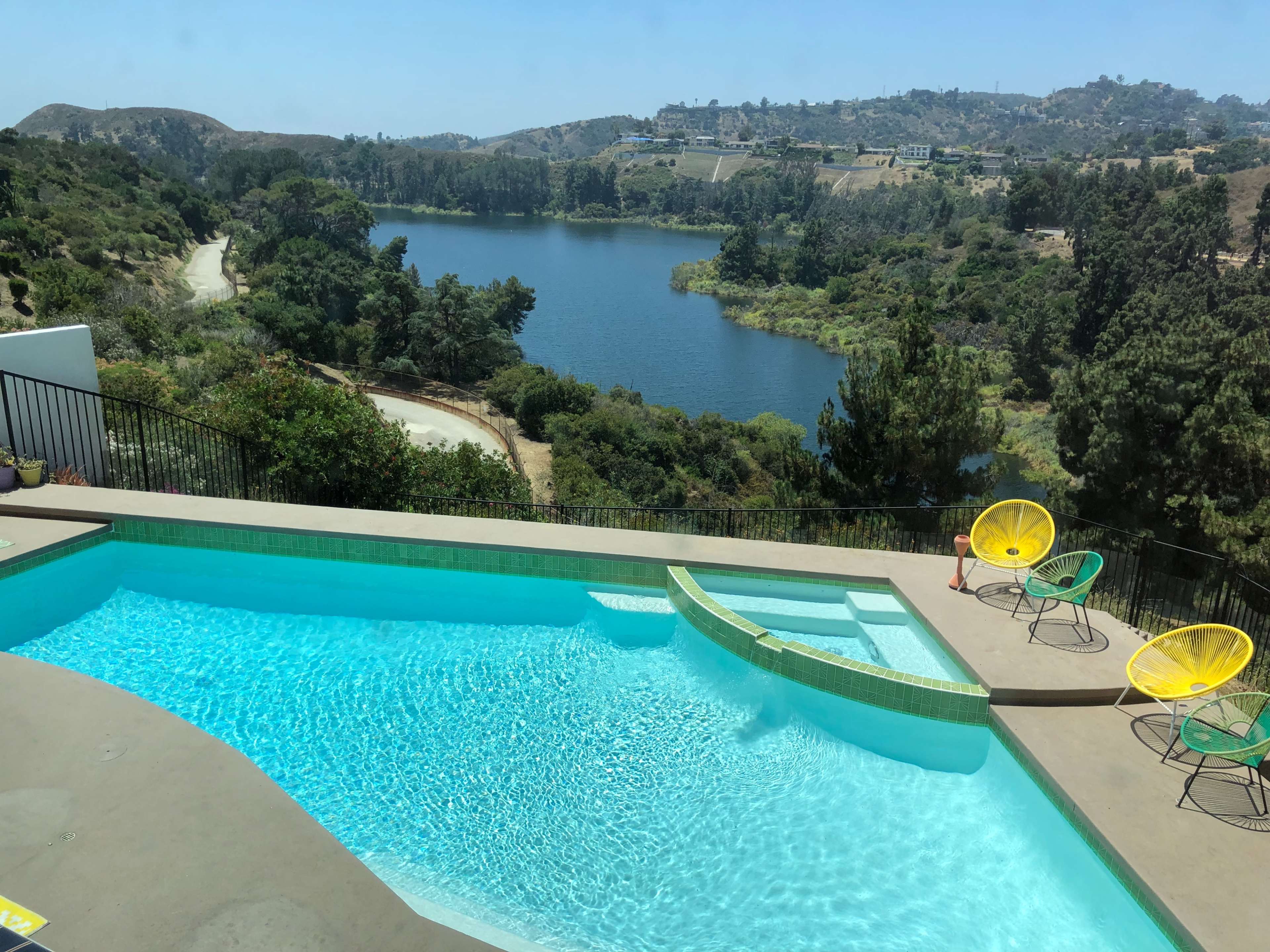 A swimming pool overlooks a calm lake surrounded by greenery and hillside.
