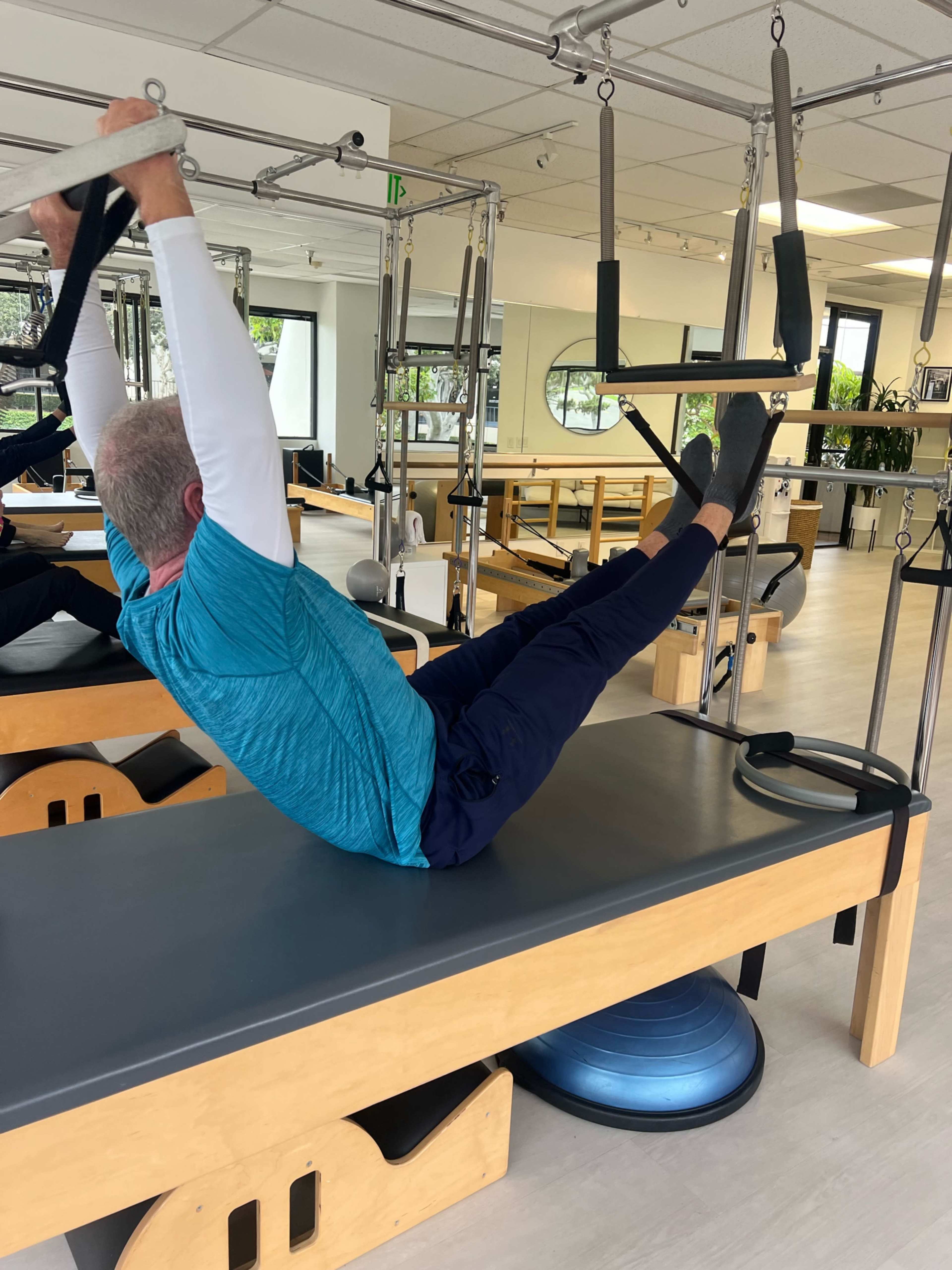 A person performs an exercise on a reformer machine in a Pilates studio.