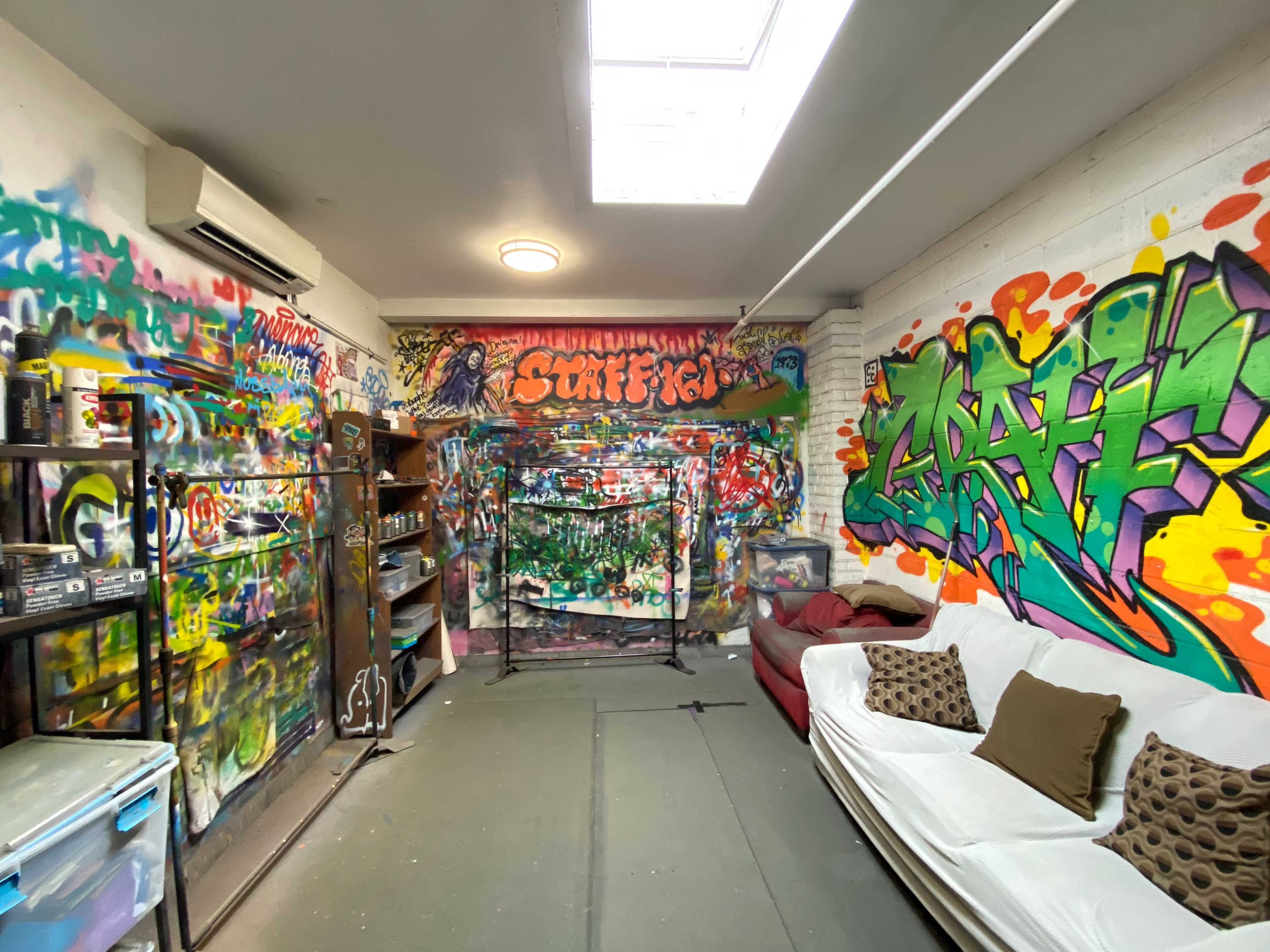 A colorful graffiti-covered room with a couch, shelves, and a backdrop for creative activities.