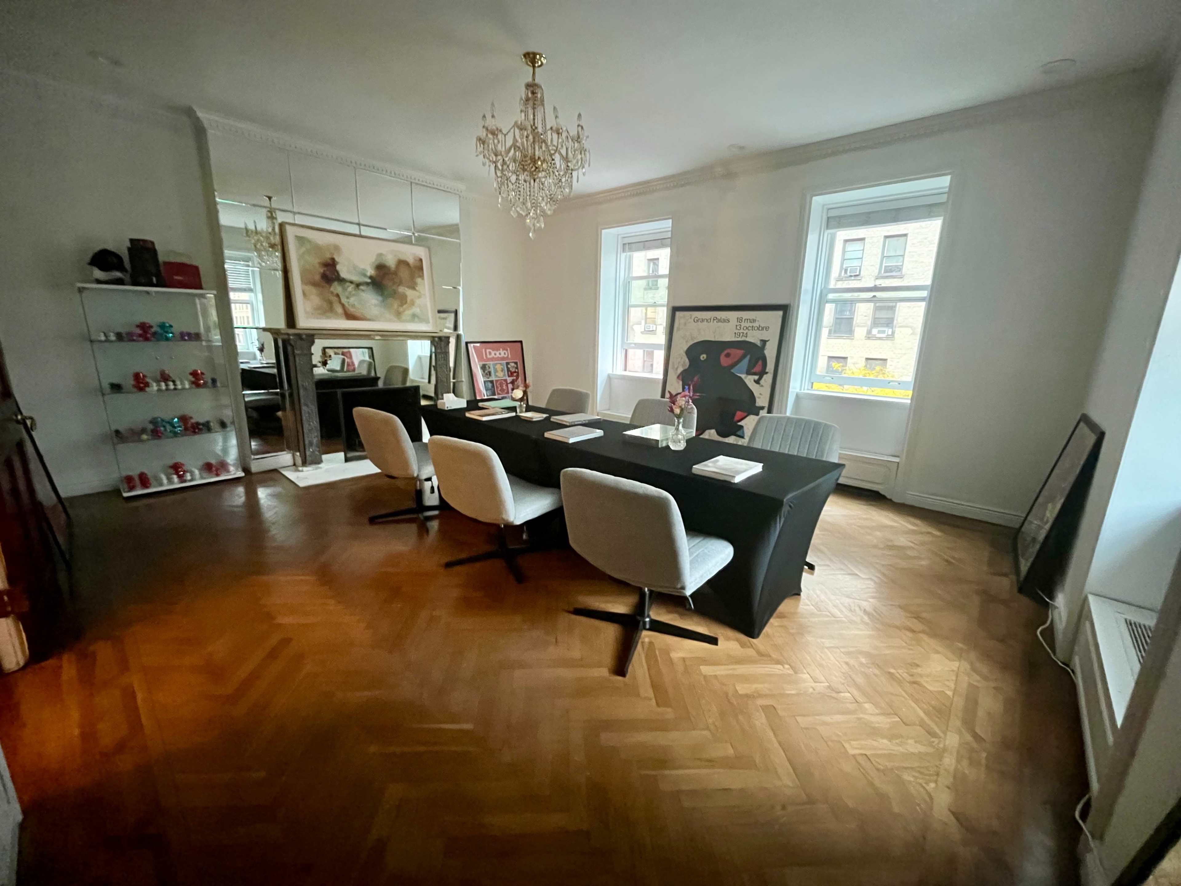 The image shows a well-lit meeting room with a rectangular table covered by a black tablecloth, surrounded by white chairs and adorned with artwork on the walls.