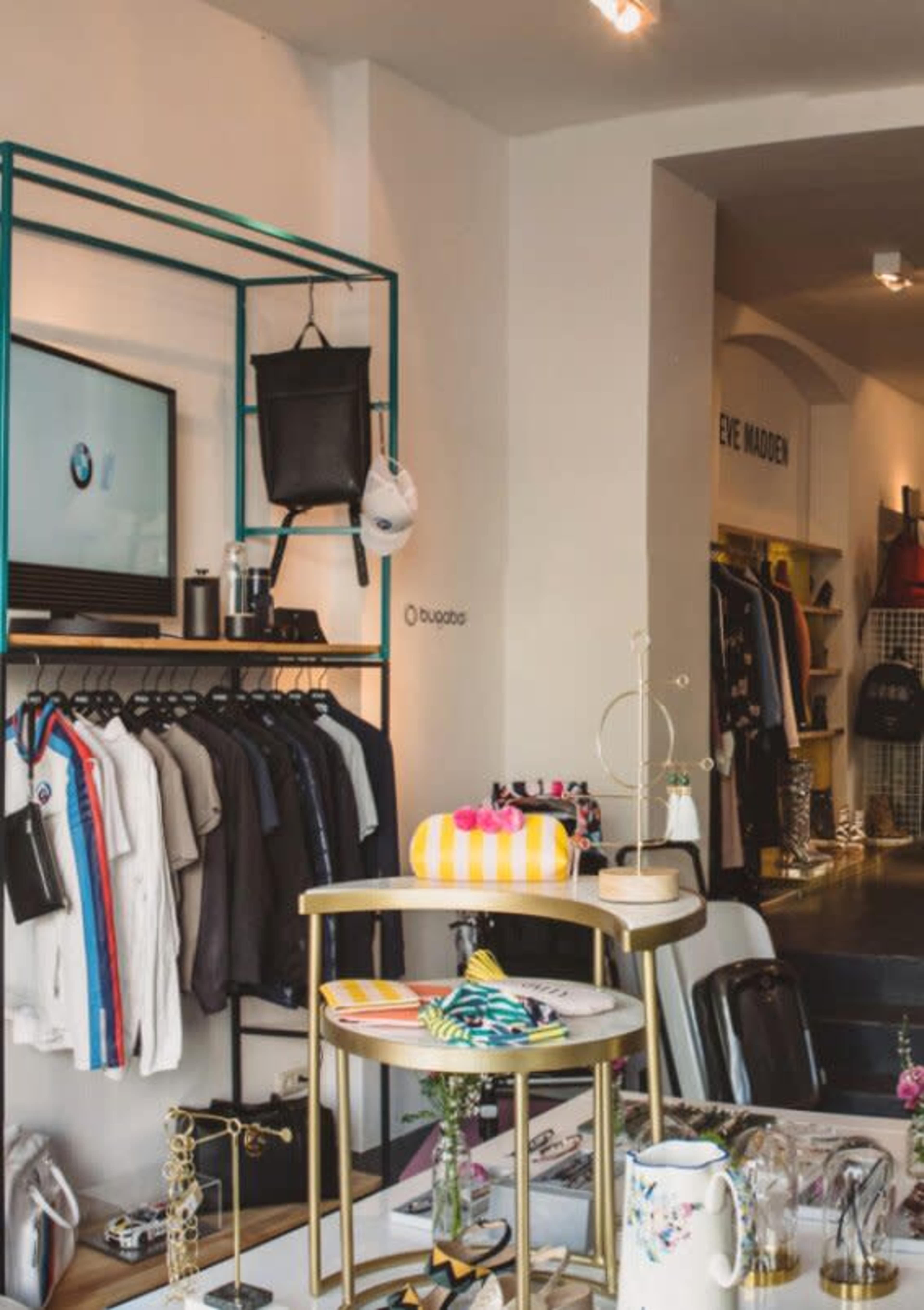 A clothing store interior featuring a display rack with various shirts, a television screen, and a table with accessories and decorative items.