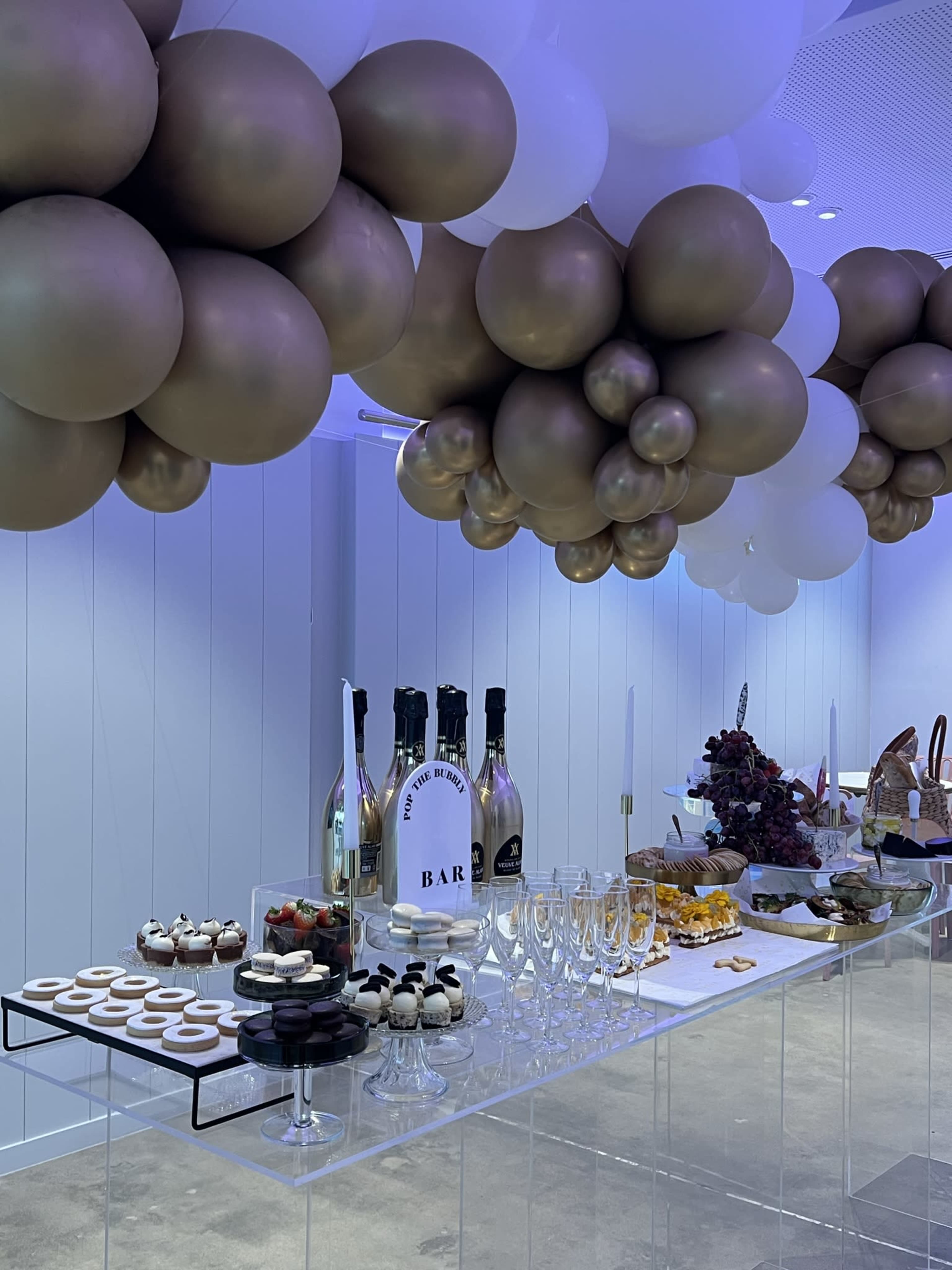 A party setup with a table featuring an array of desserts and drinks, topped with decorative balloons.