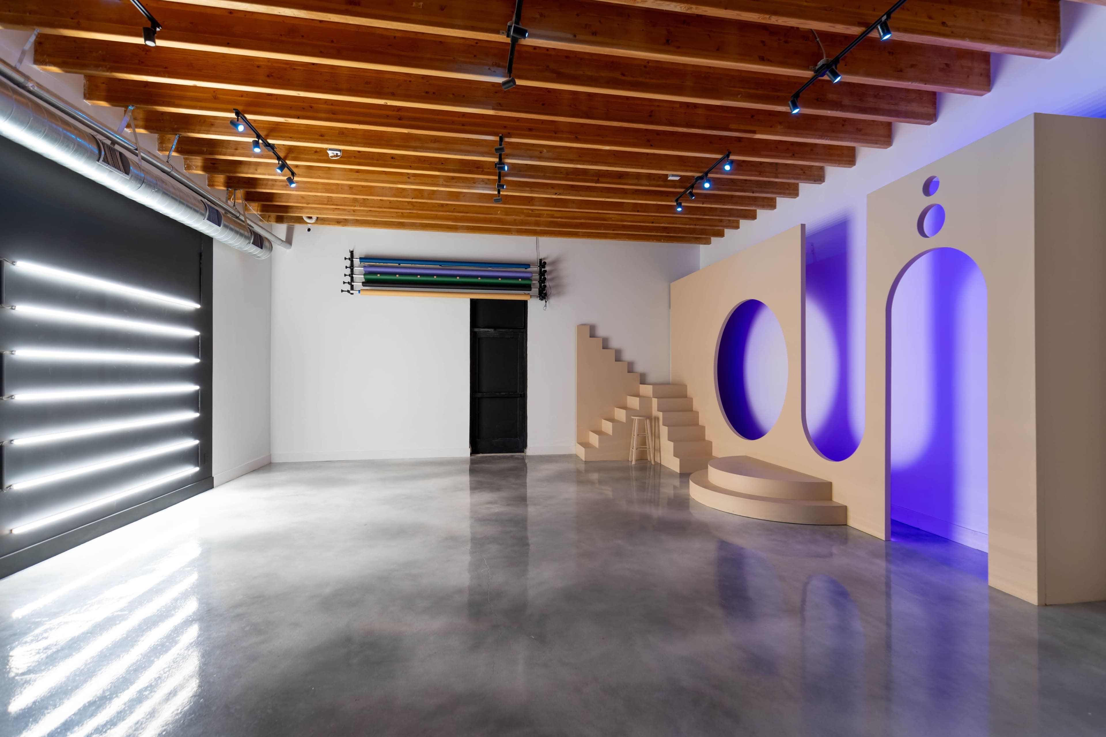 A modern interior space with wooden beams, concrete flooring, and a minimalist design featuring geometric shapes and built-in lighting.