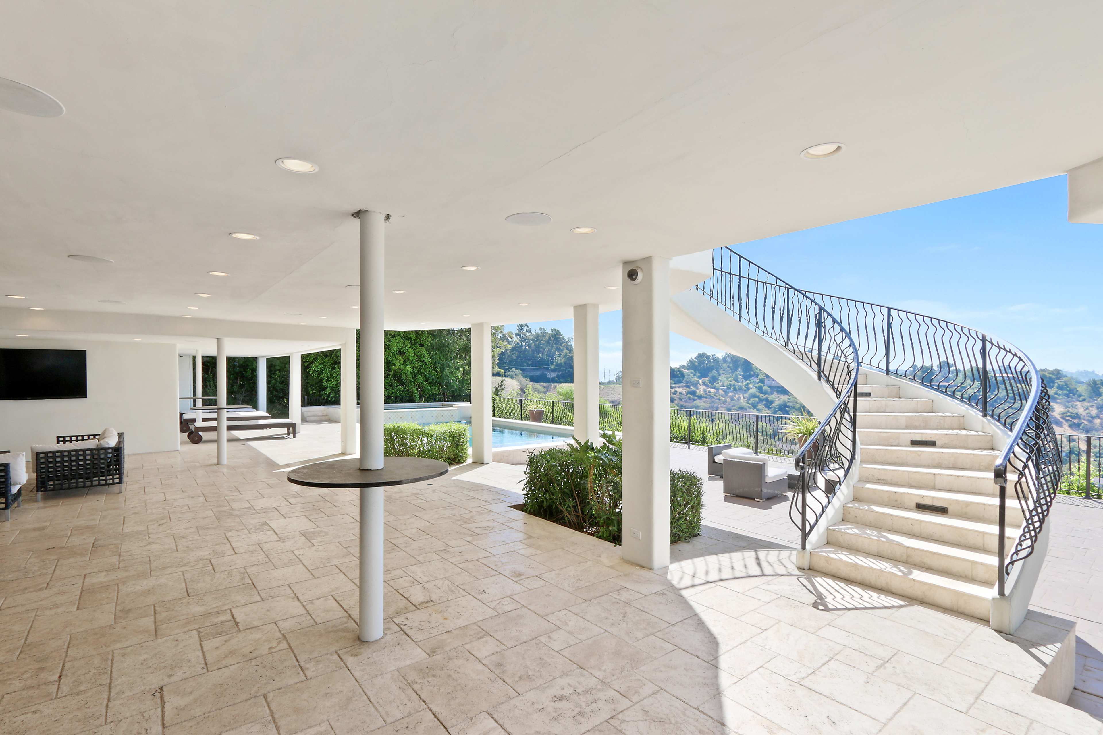 A spacious outdoor terrace with a swimming pool and a curved staircase leading to an upper level.