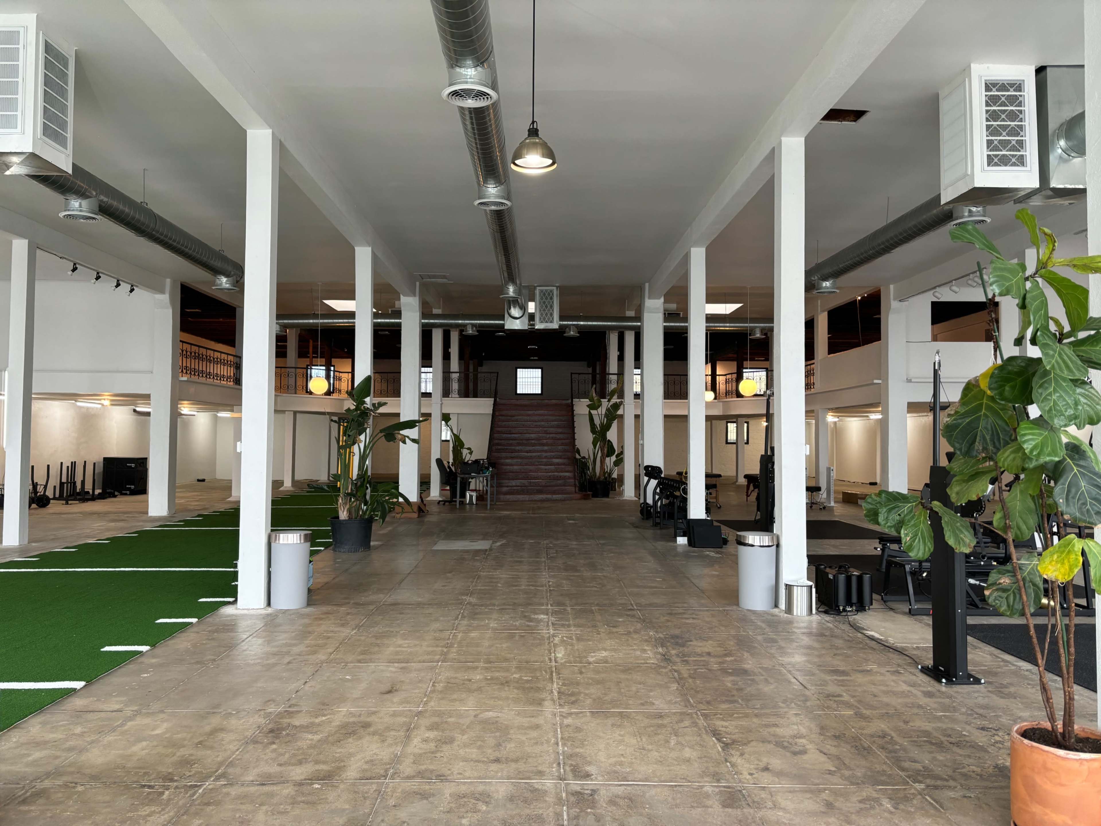 A spacious, open gym area with a carpeted turf section and various fitness equipment arranged along the sides.