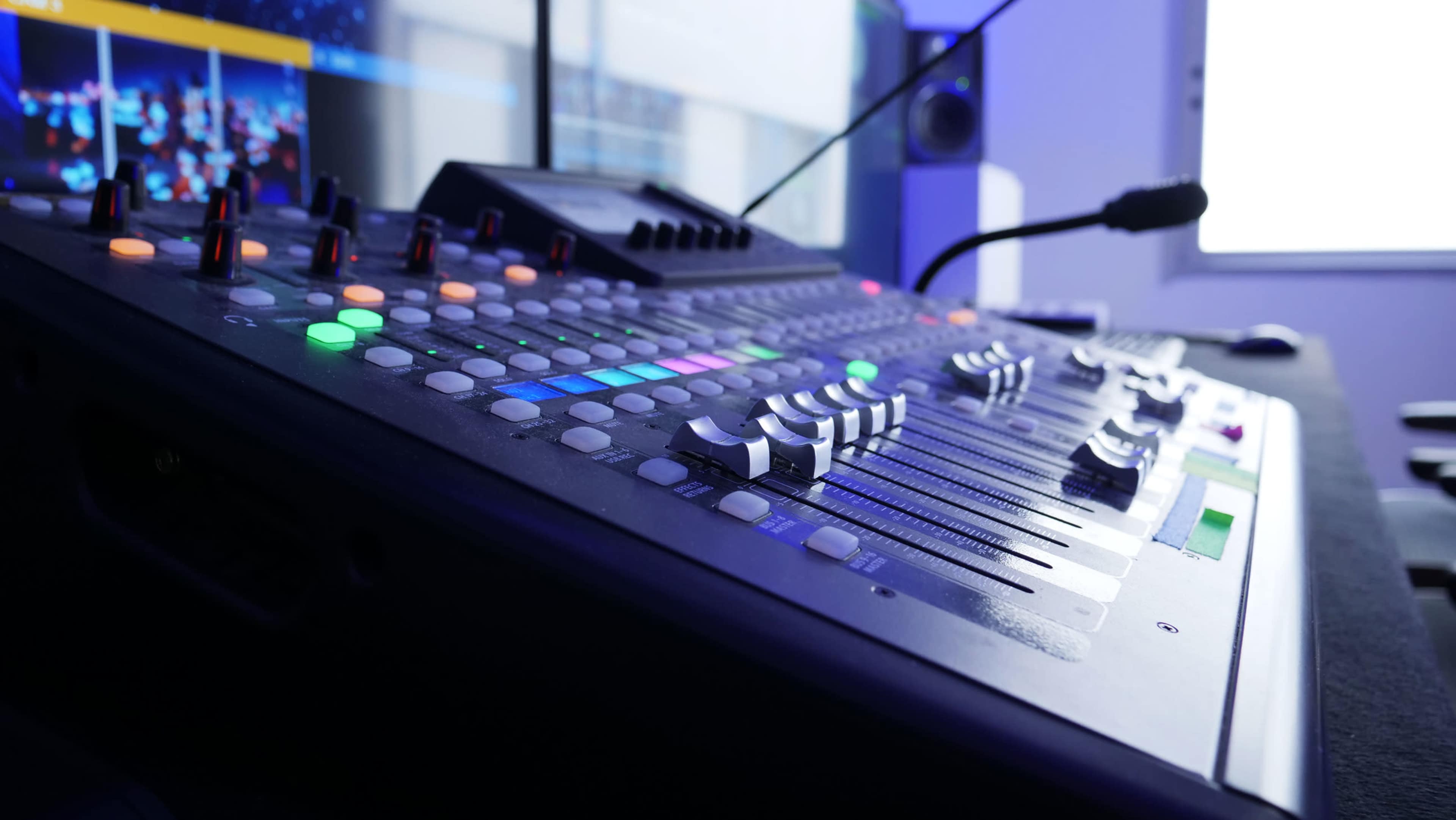 A close-up of a digital audio mixing console featuring colorful buttons and sliders, set in a modern studio environment.