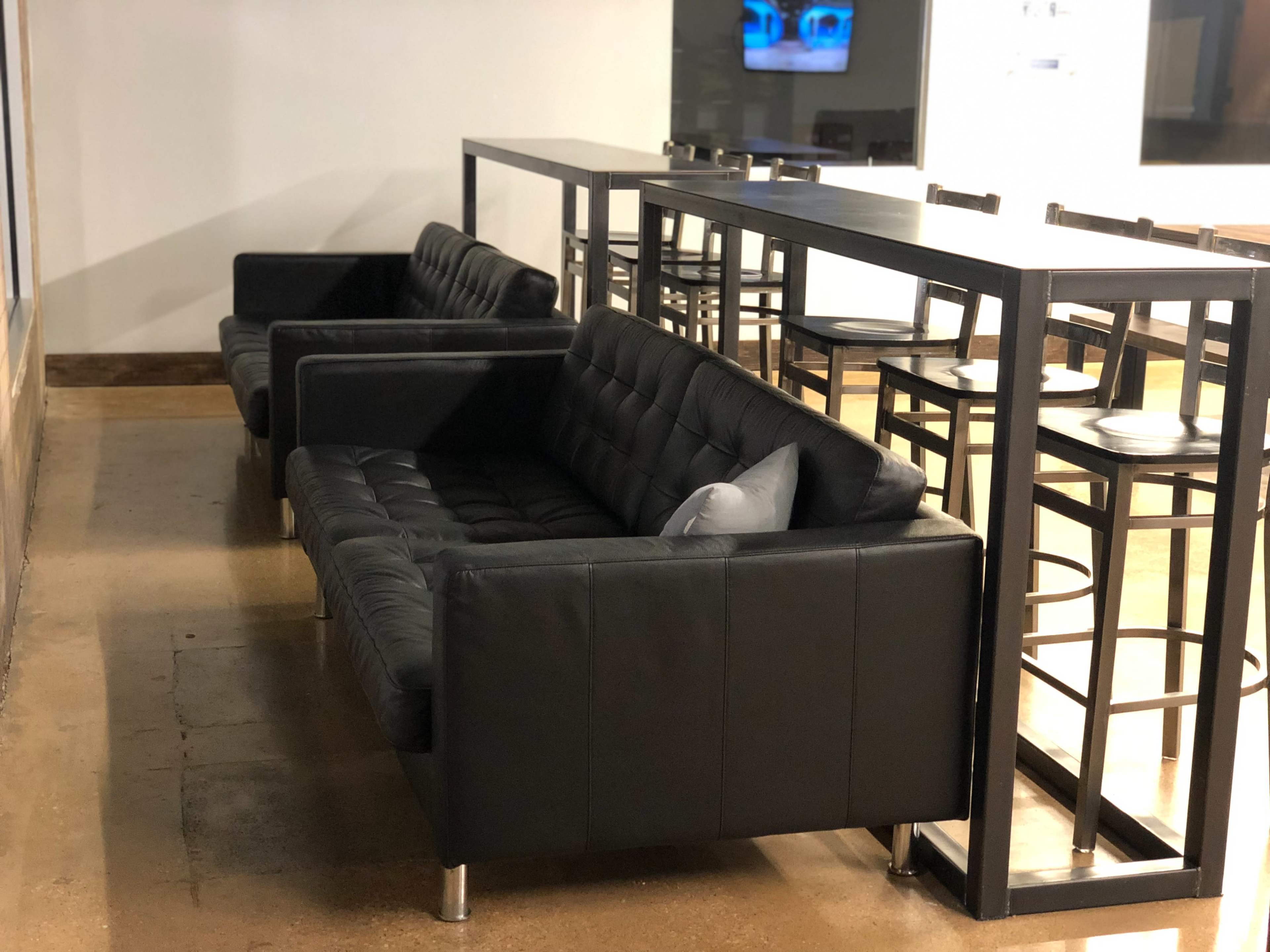 Two black sofas are placed alongside a high table with bar stools in an indoor space.