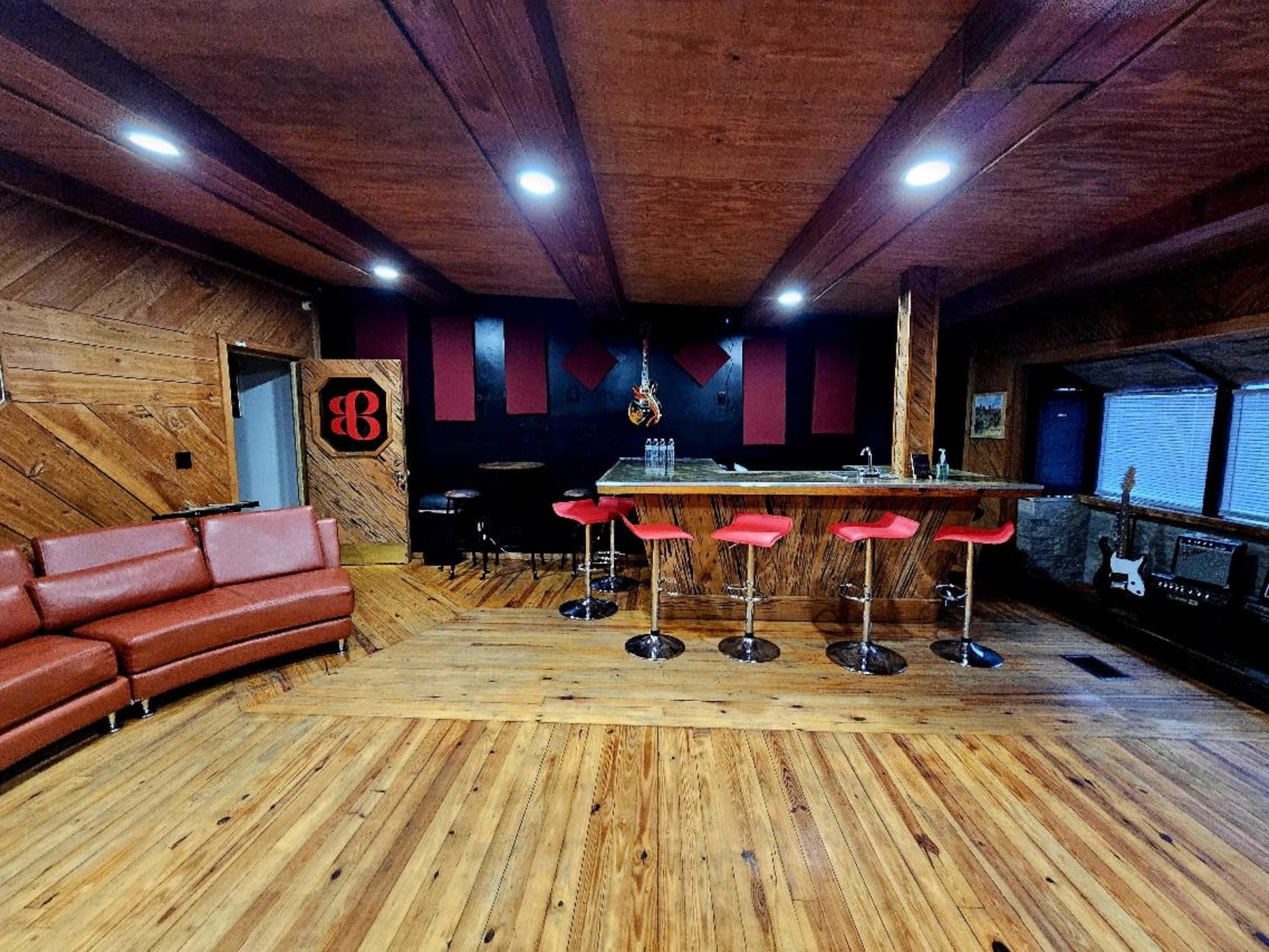 The image shows a stylish interior featuring a wooden floor, a modern bar with red stools, and a large, comfortable red couch.