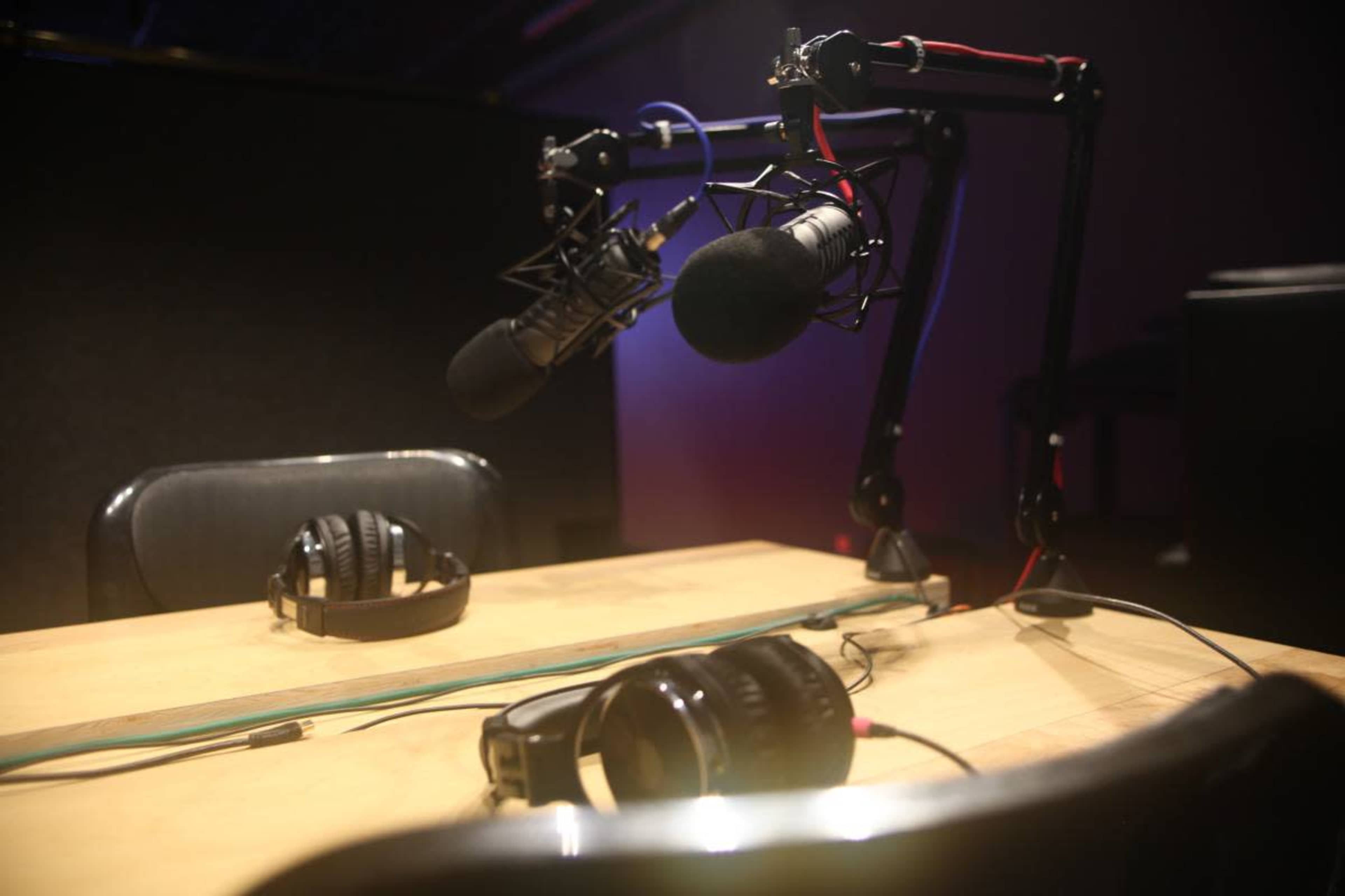 A wooden table is set with two pairs of headphones and two microphones mounted on adjustable arms.