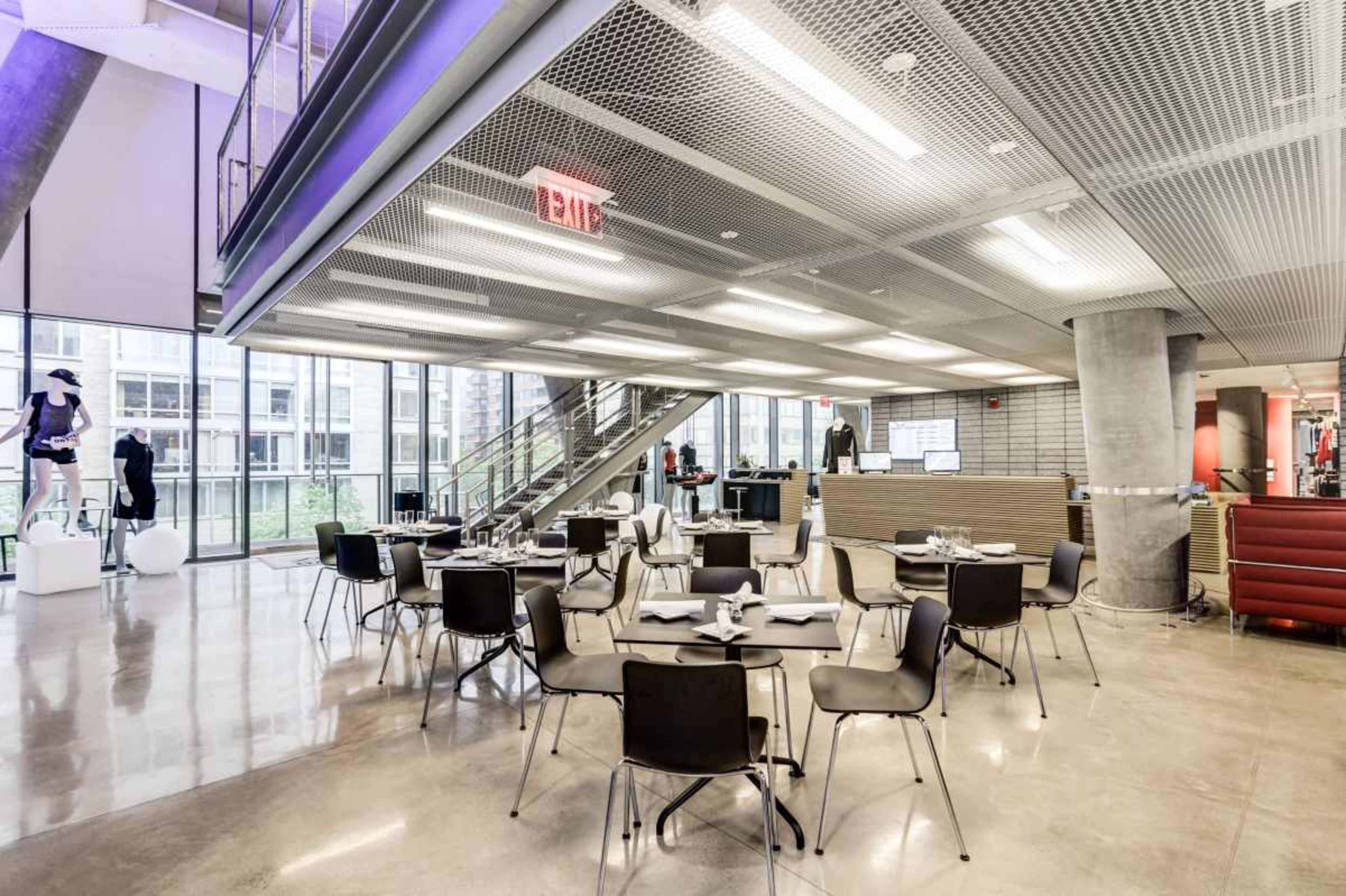 A modern dining area features tables and chairs arranged around a spacious layout with large windows and polished concrete floors.