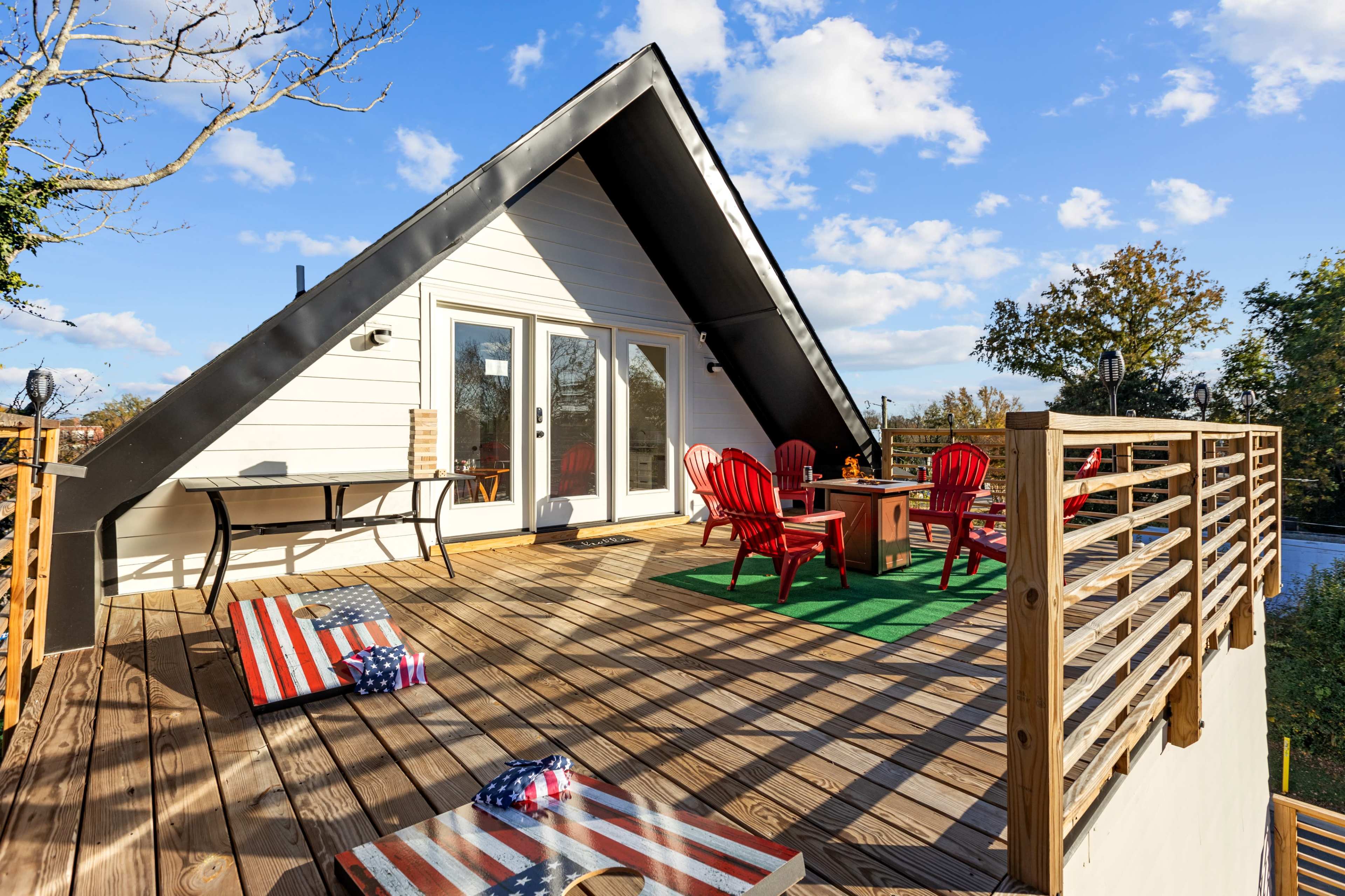 A wooden deck with red Adirondack chairs and a small table, leading to glass doors of a house beneath a sloped roof.