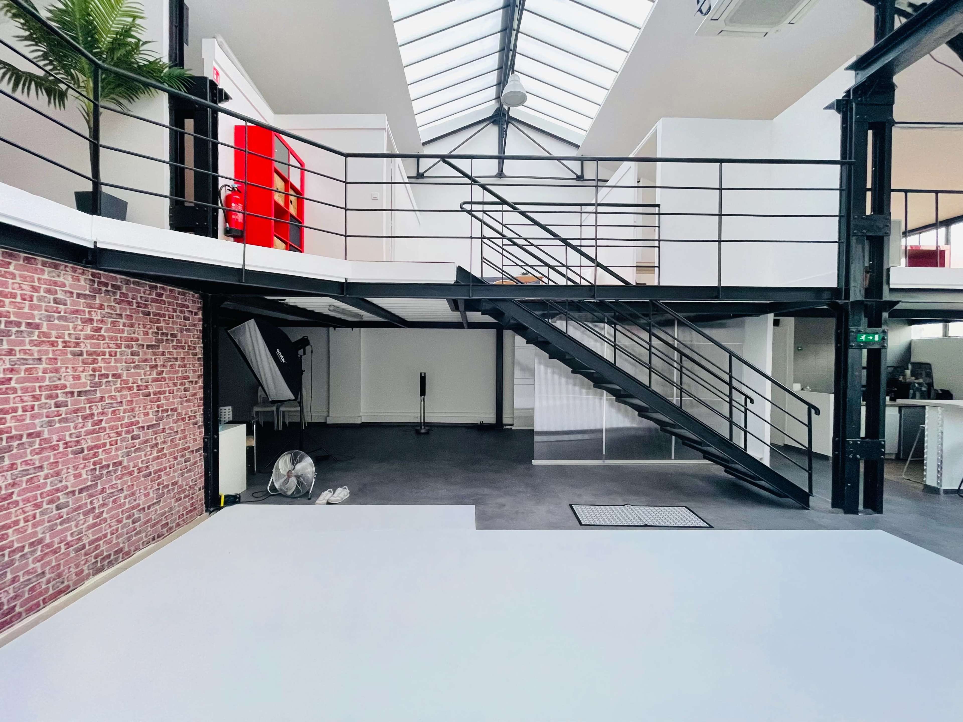 A modern, open-concept space with a mezzanine, featuring a red door, brick wall accents, and industrial-style stairs.