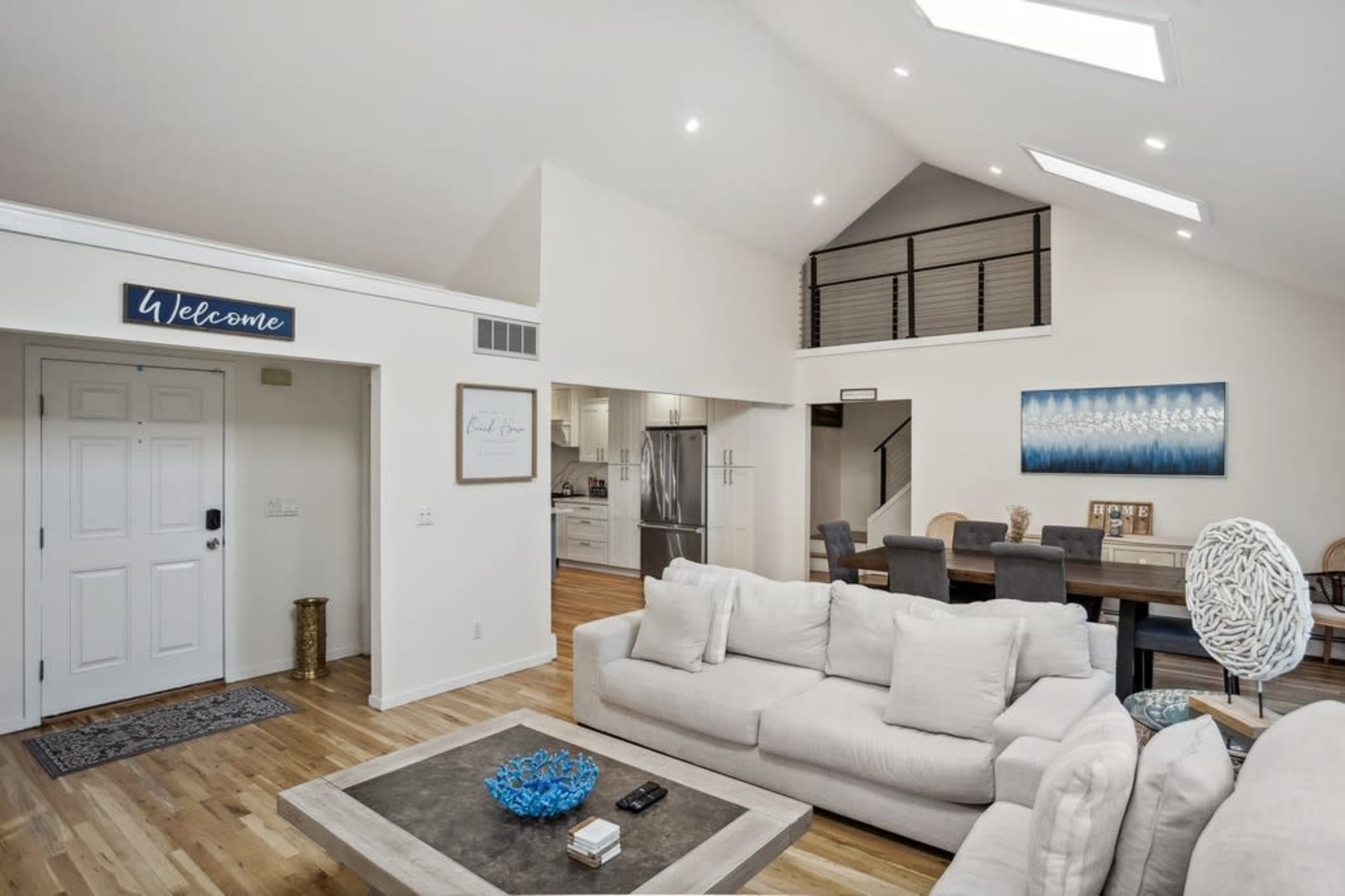 The image shows a spacious living area featuring a light-colored sectional sofa, a coffee table, and an open layout that connects to a dining area.