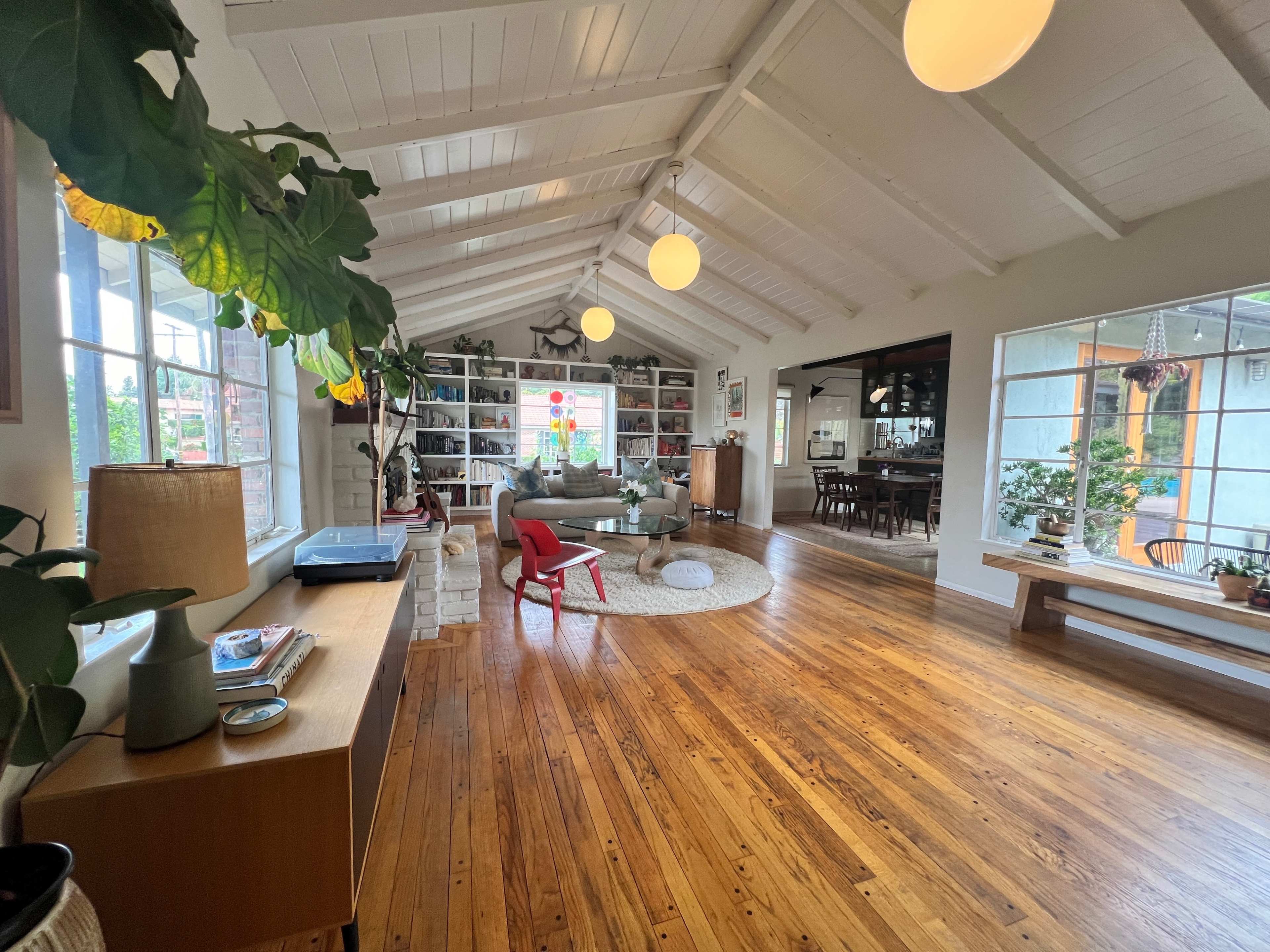 A spacious, well-lit living area with wooden floors, vaulted ceilings, and a mix of modern furniture and decor.