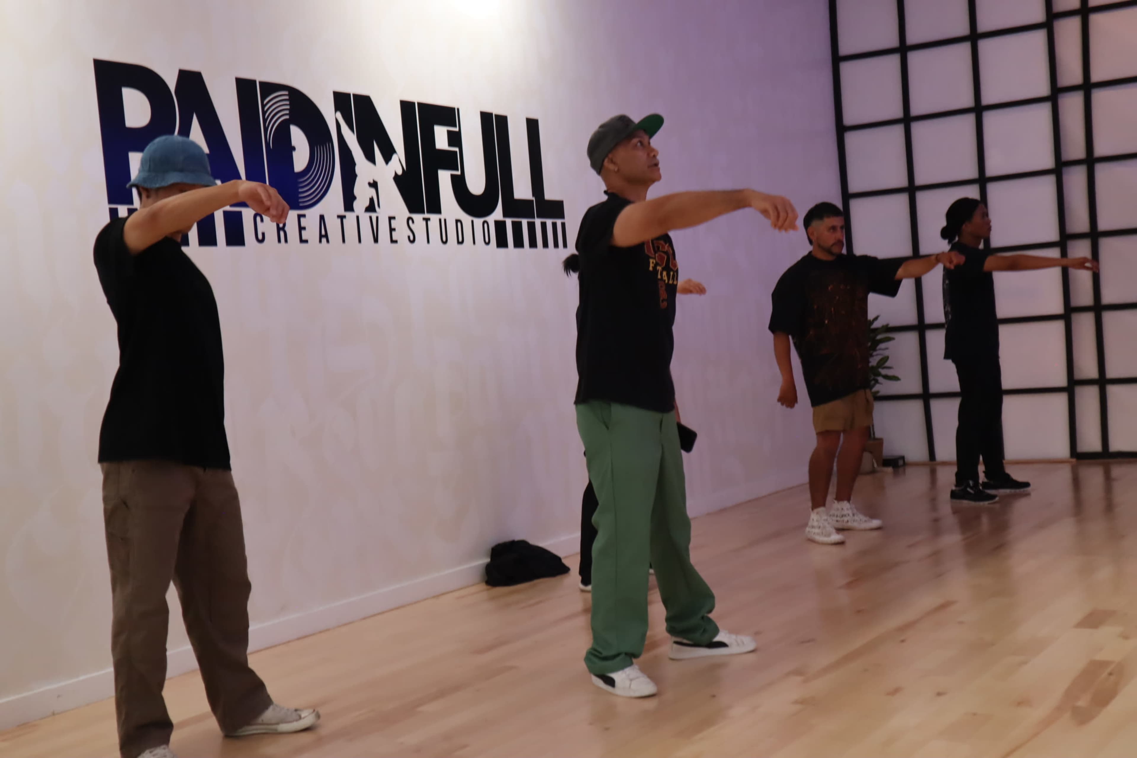 A group of four people performs a dance routine in a studio with the words "RADIN FULL" displayed on the wall.