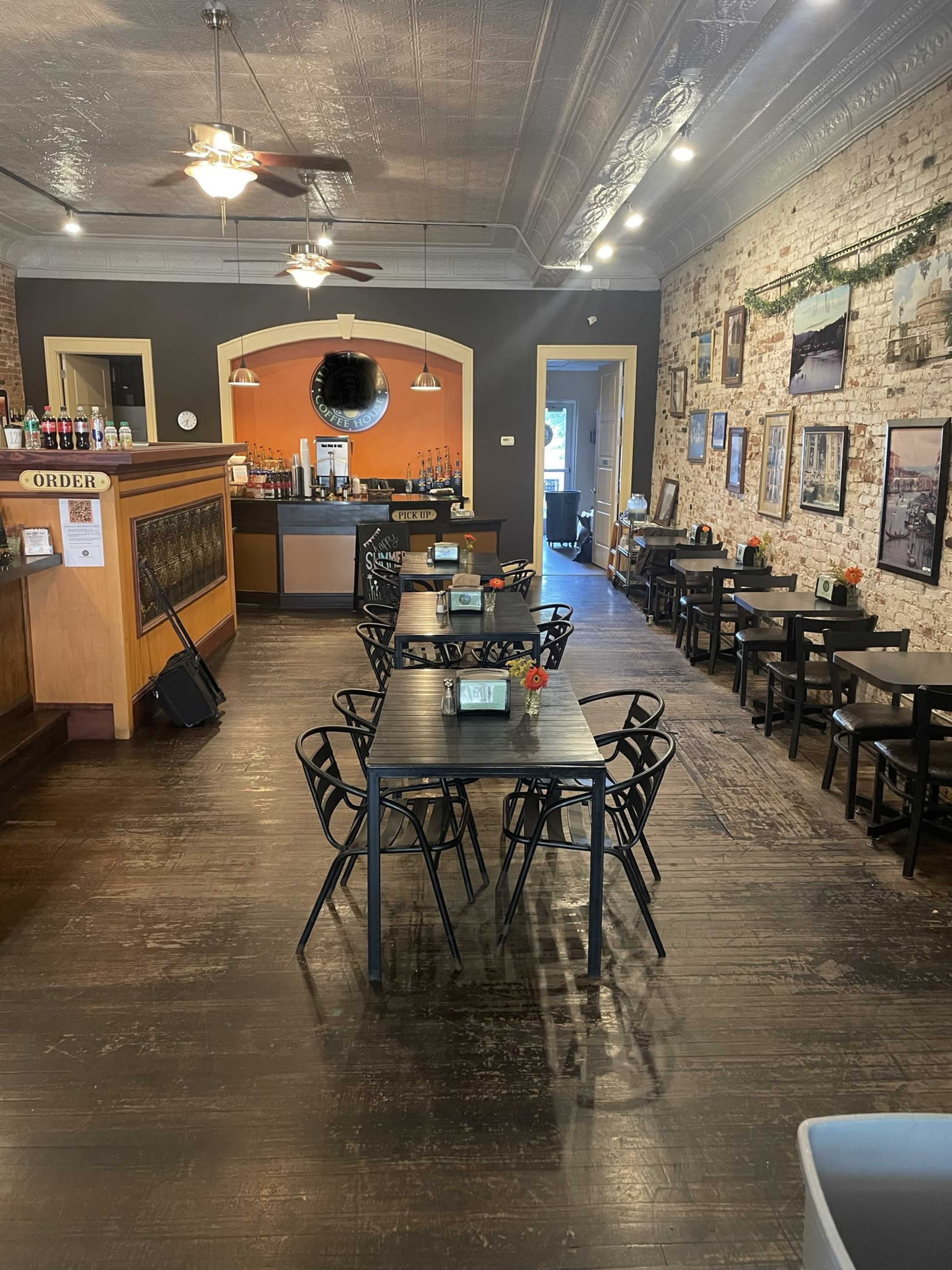 A spacious café with wooden floors, tables arranged for dining, and a counter in the back area.