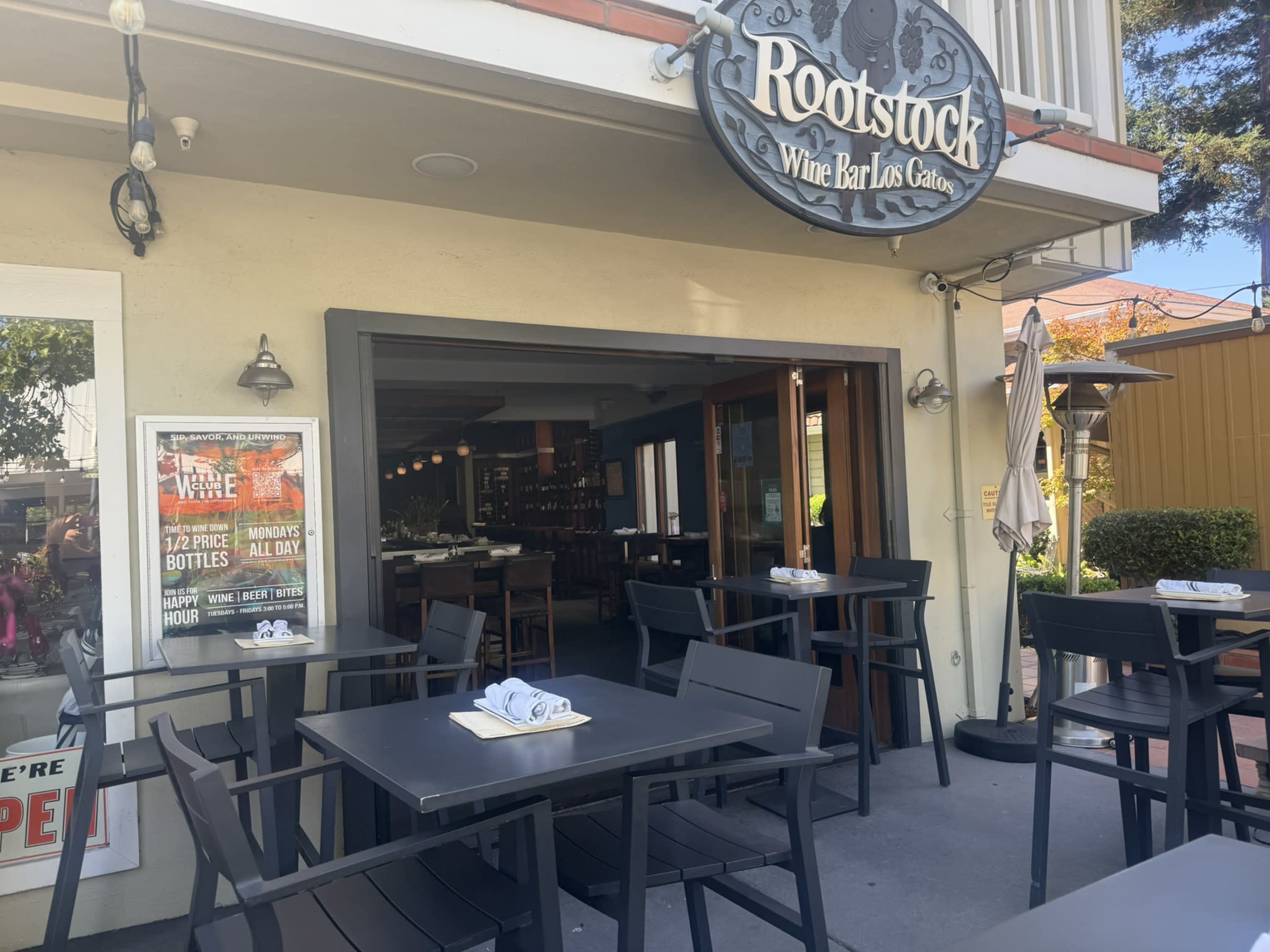 The image shows the entrance to a wine bar named Rootstock, featuring outdoor seating and a large sign above the door.