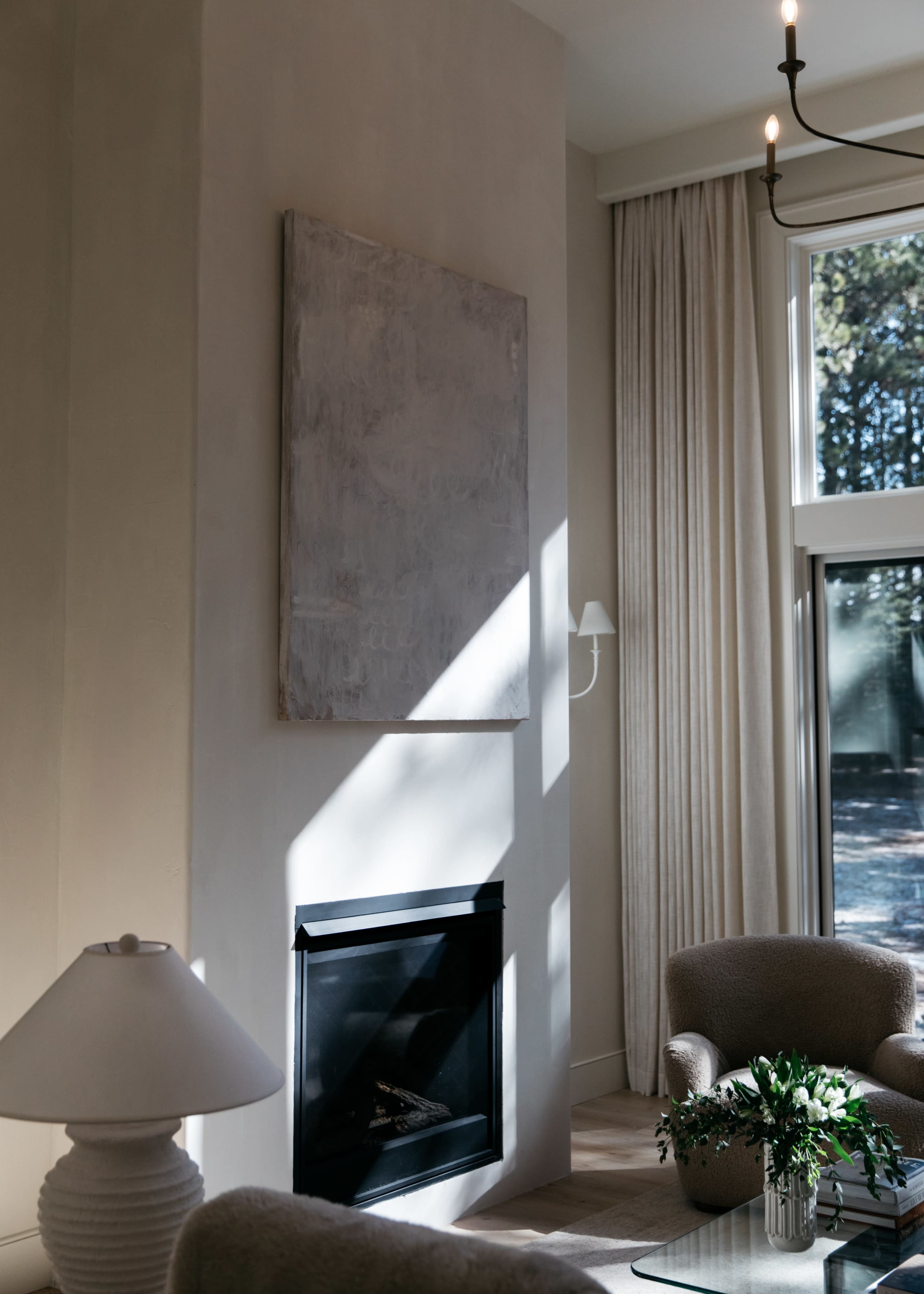 A living room with a modern fireplace, a large piece of abstract art on the wall, and a pair of armchairs beside a coffee table, illuminated by natural light.